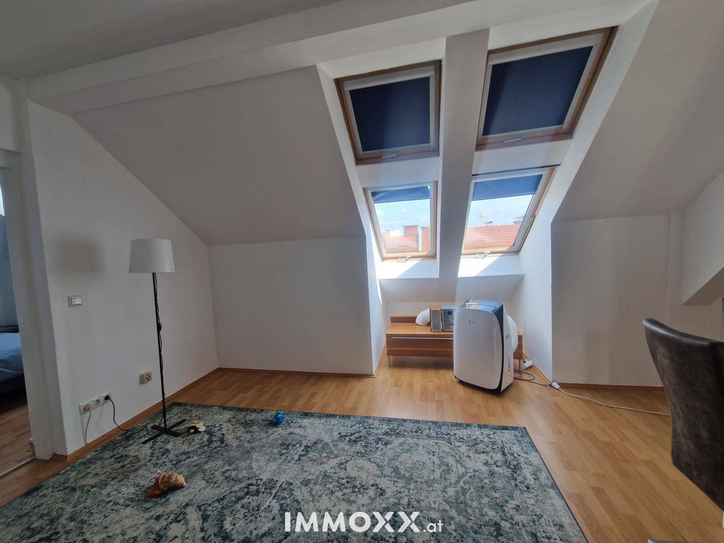 Heller Wohnbereich mit Holzboden, Teppich und mehreren Dachfenstern unter der Dachschräge.