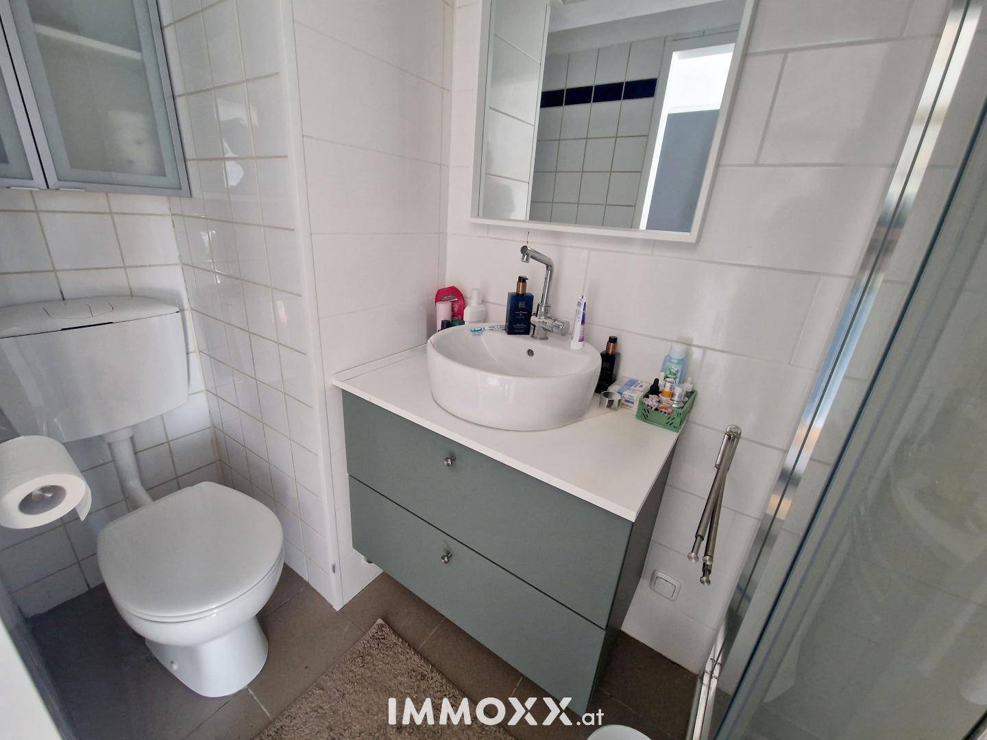 Modernes Badezimmer mit WC, Waschbecken, Spiegelschrank und Duschbereich, hell gefliest.