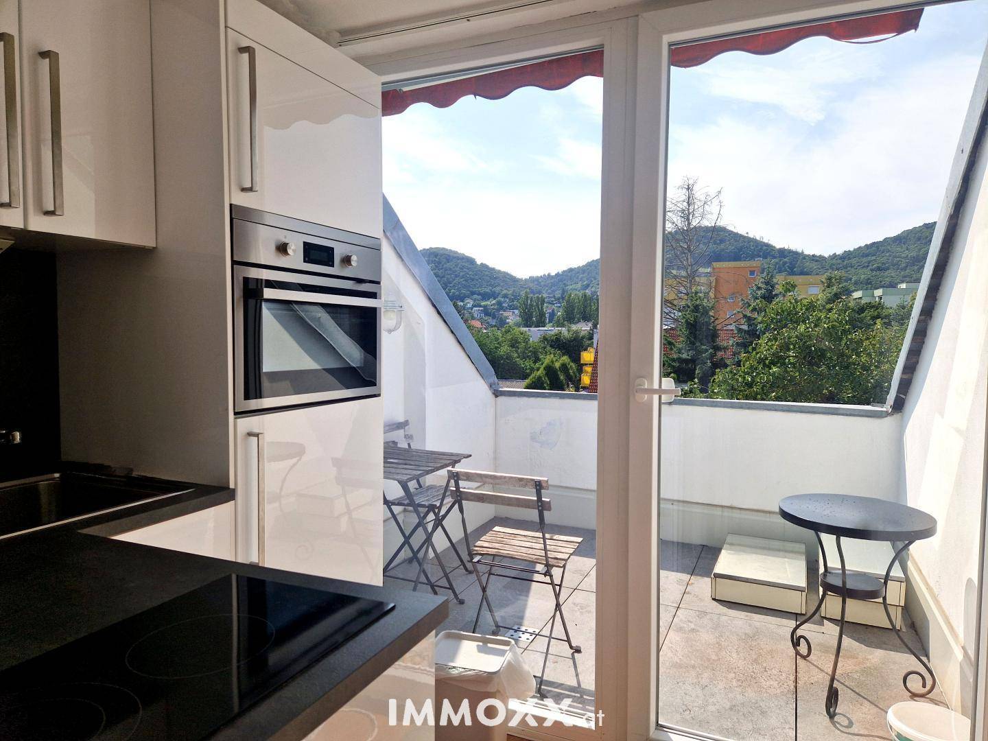 Moderne Küchenzeile mit Blick auf die grüne Umgebung und die möblierte Dachterrasse.