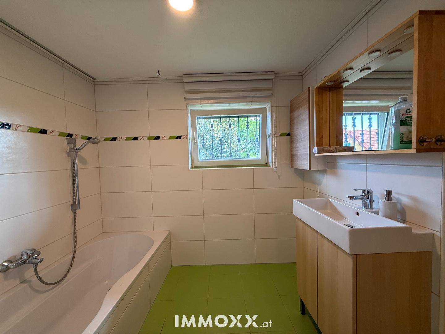 Badezimmer mit Badewanne, Waschbecken, Spiegelschrank und Fenster.