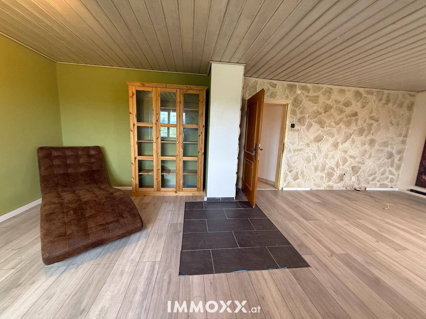 Heller Wohnbereich mit Holzboden, grüner Akzentwand und rustikaler Steinwand.