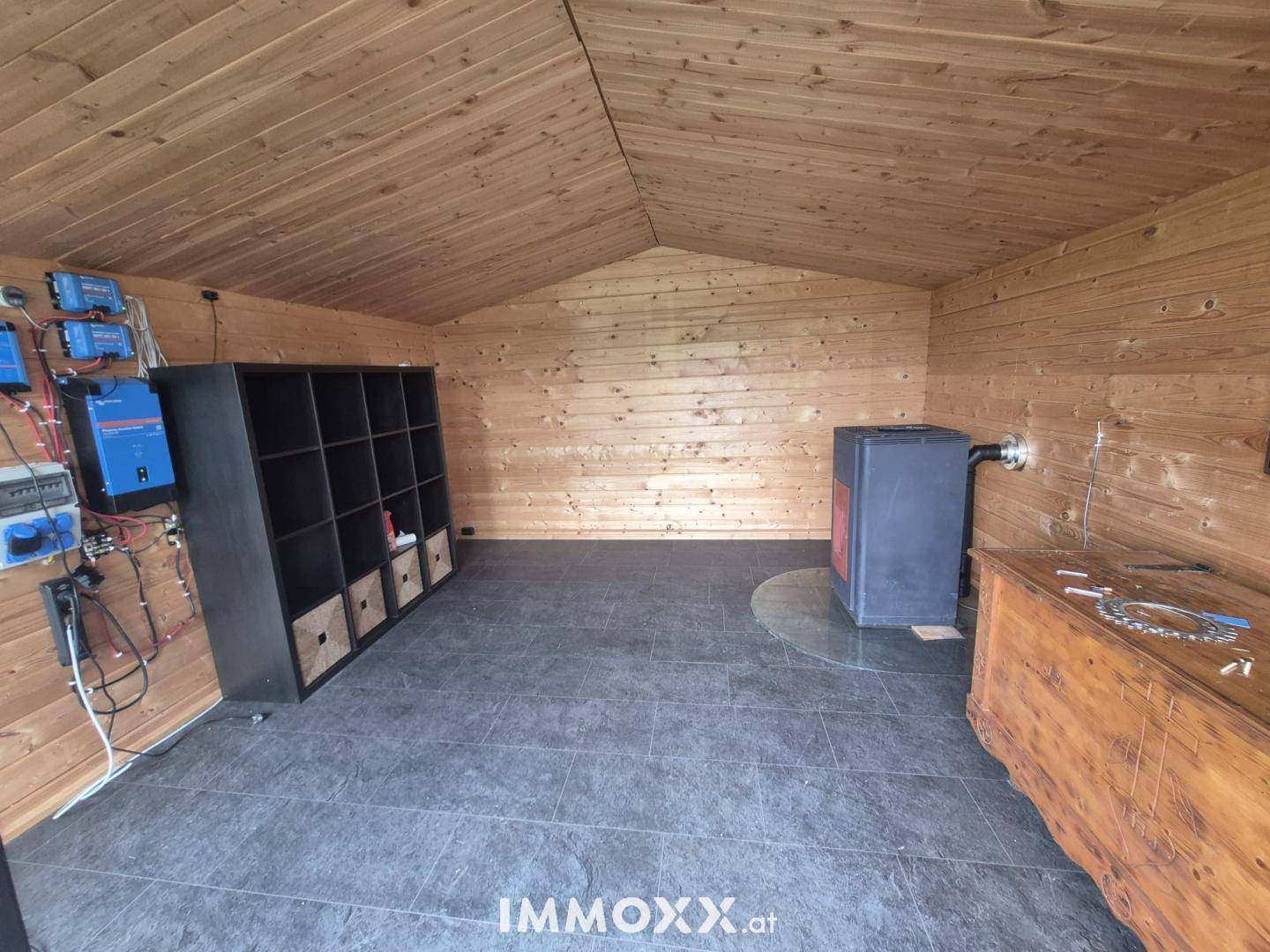 Innenraum eines Holzhauses mit Holzverkleidung, Regalen und einem Ofen.