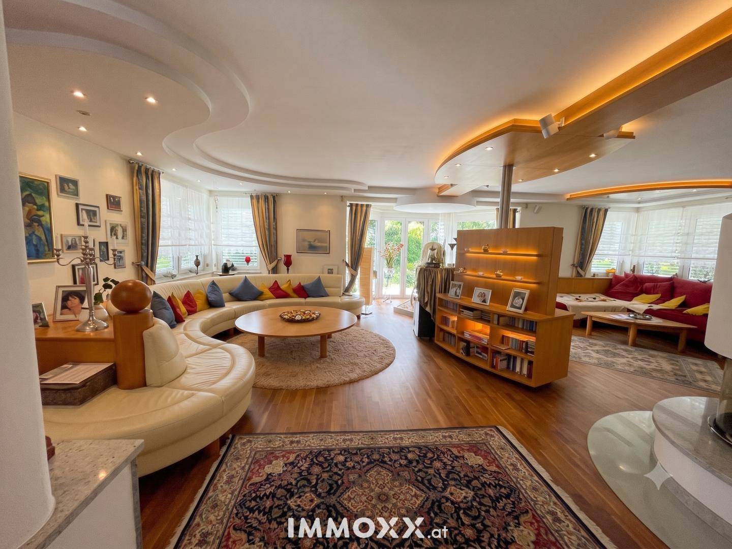 Geräumiges Wohnzimmer mit bequemen Rundsofas, Holzboden und indirekter Deckenbeleuchtung.