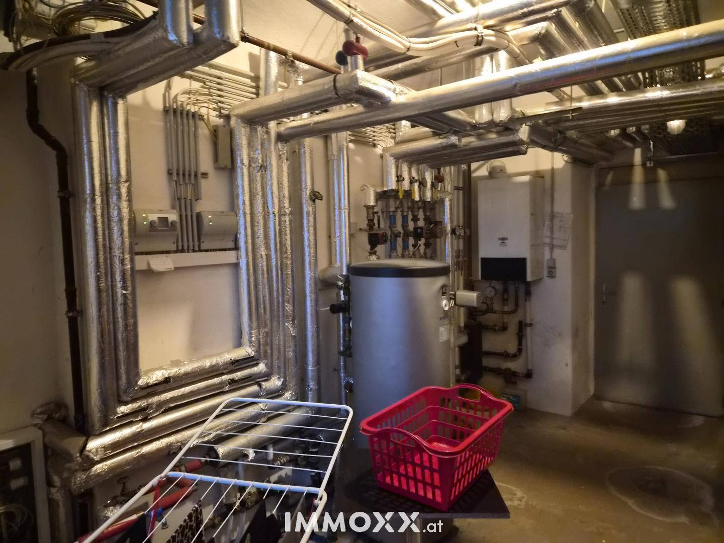 Technikraum mit Heizungsanlagen, Warmwasserspeicher und zahlreichen Rohrleitungen im Keller.