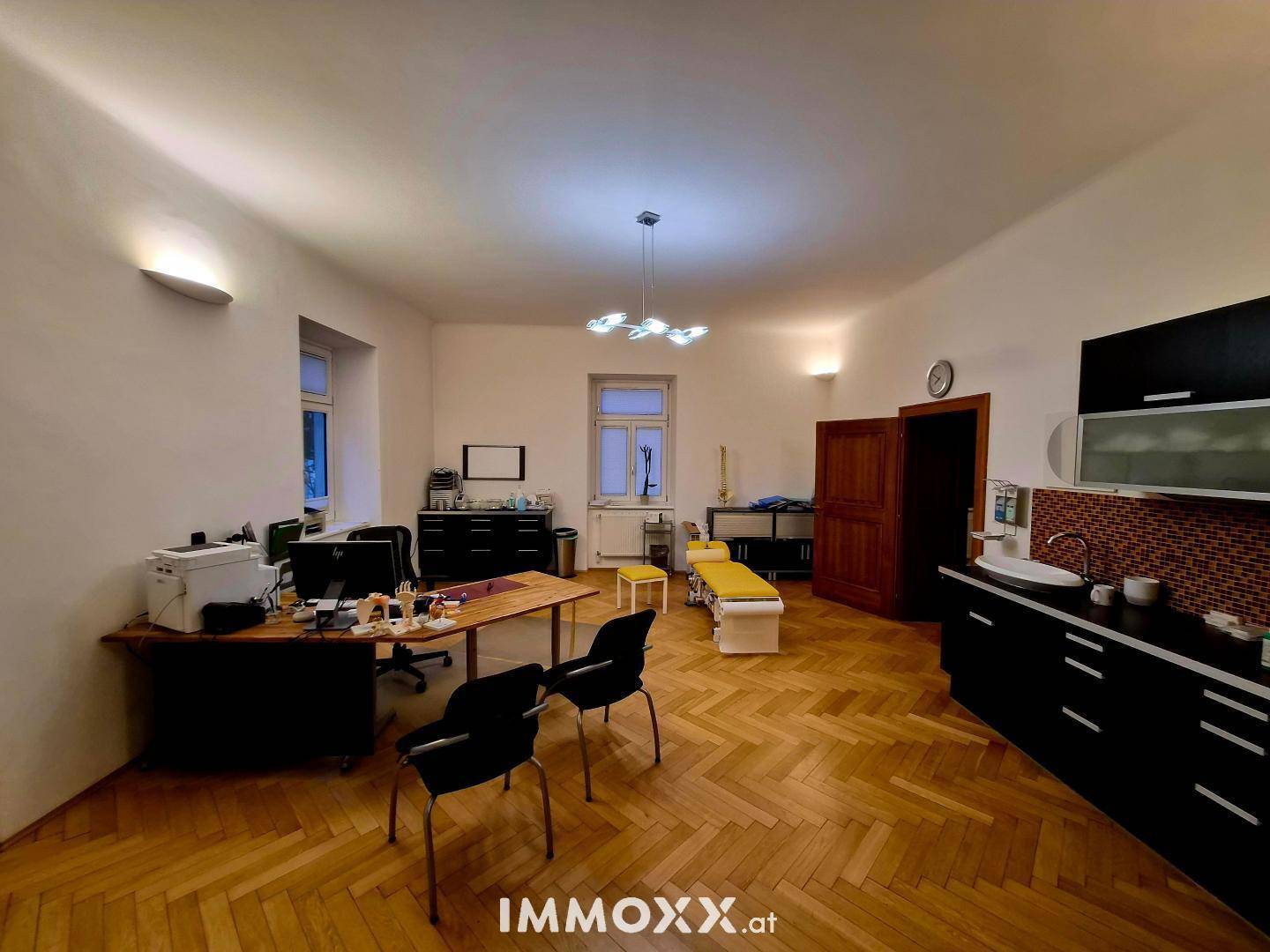 Geräumiges Büro oder Behandlungszimmer mit Parkettboden und integrierter Küchenzeile.