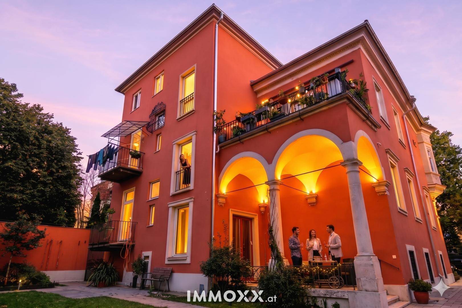 Abendliche Ansicht der Villa mit beleuchteter Fassade und geselligem Außenbereich unter Arkaden.