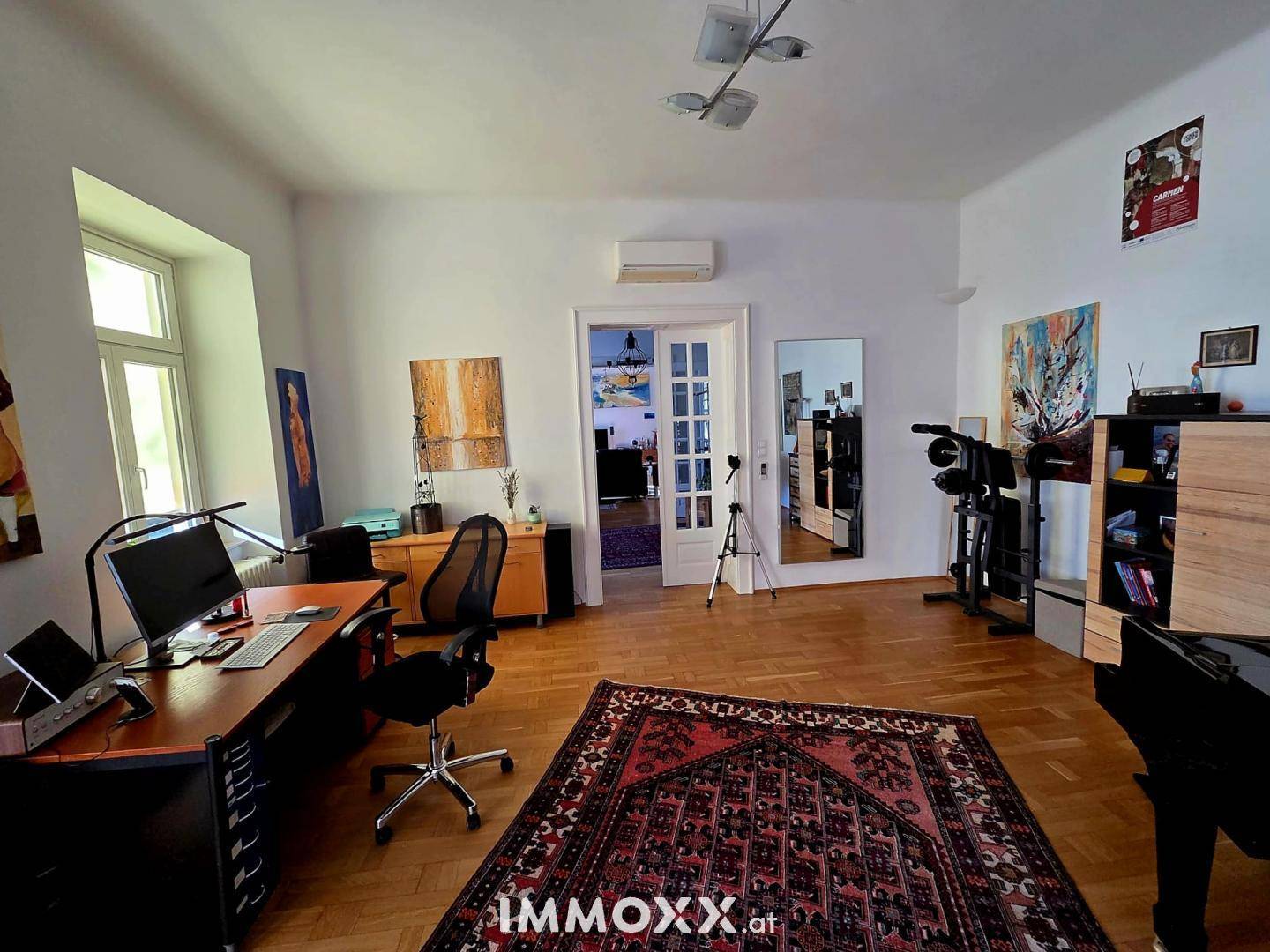 Helles Arbeitszimmer mit Parkettboden, großem Schreibtisch und dekorativen Elementen.