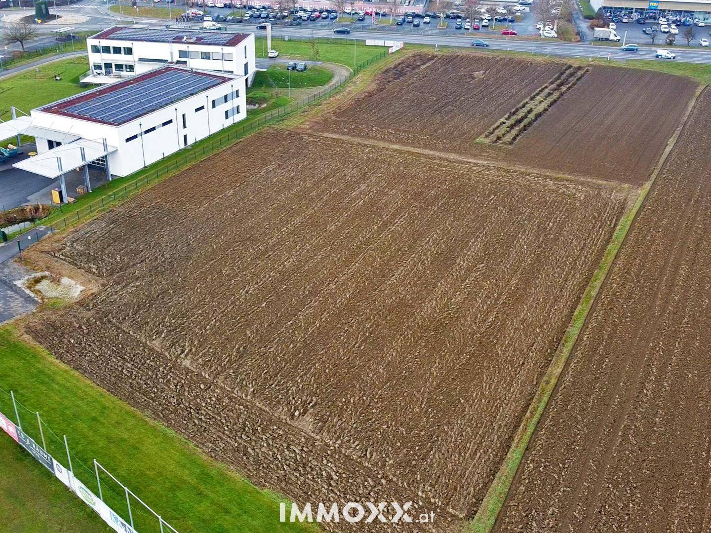 Übersicht aus der Luft zeigt ein großes Ackerland, ein Gebäude mit Solaranlage und einen Sportplatz.