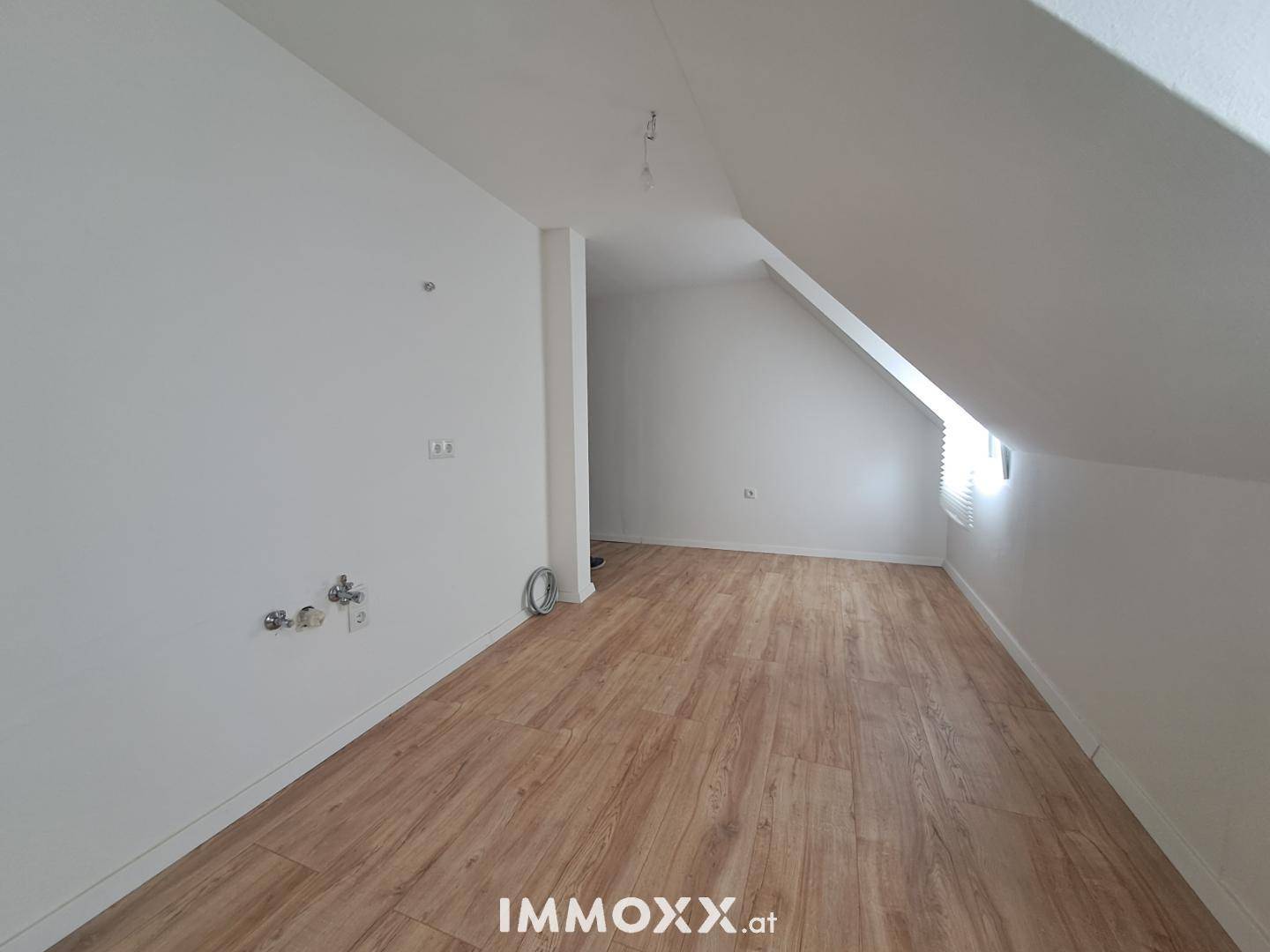 Geräumiger Dachgeschossraum mit Laminatboden, weißen Wänden und vorbereiteten Anschlüssen.
