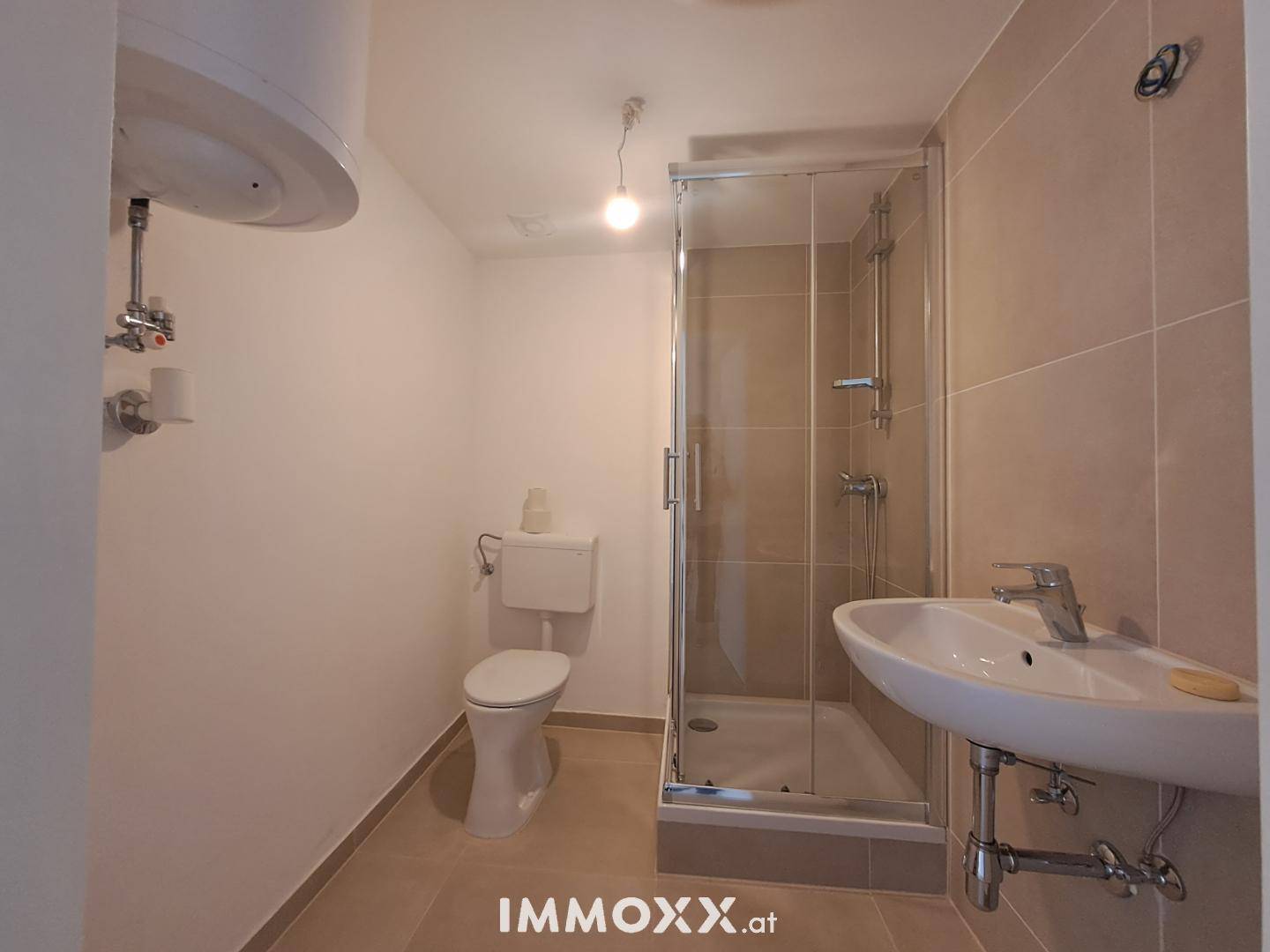 Funktionales Badezimmer mit Duschkabine, WC, Waschbecken und Warmwasserboiler.