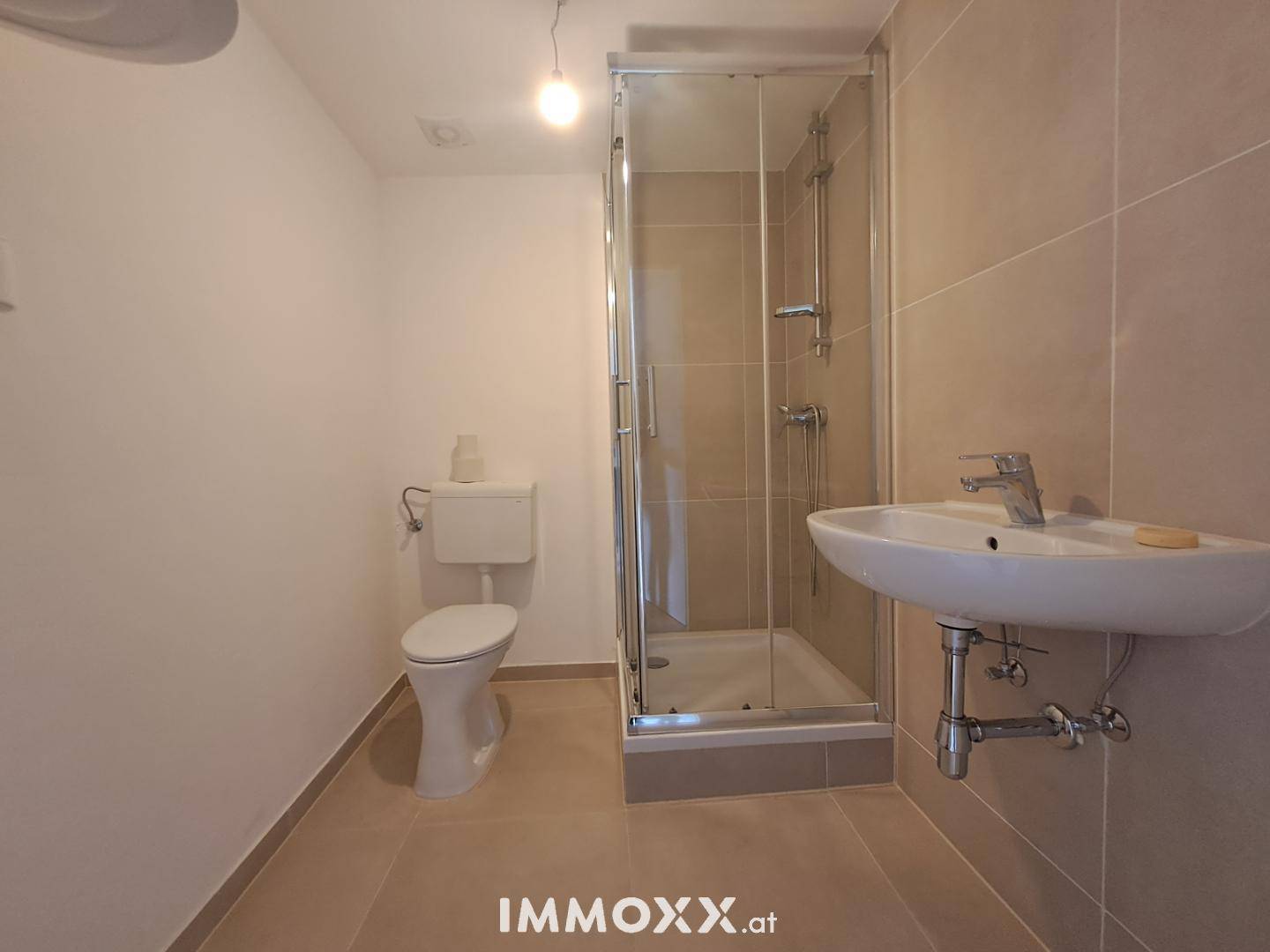 Modernes Badezimmer mit Duschkabine, WC und Waschbecken in hellen Beigetönen.