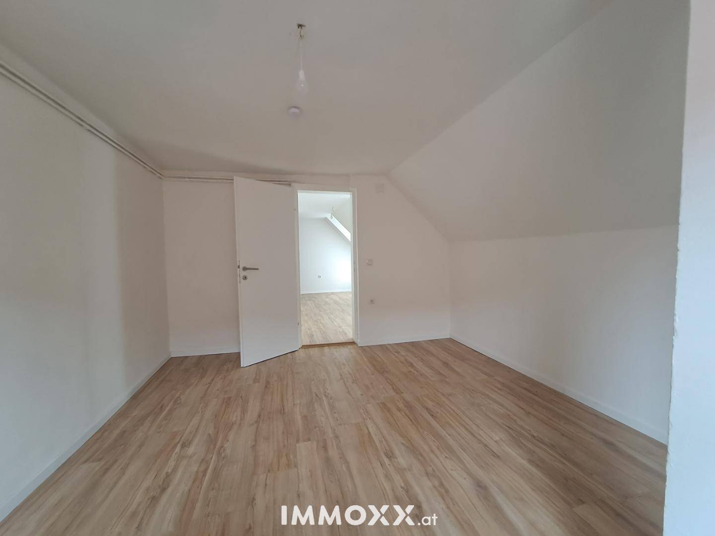 Heller, leerer Raum im Dachgeschoss mit Laminatboden und Zugang zu einem weiteren Zimmer.