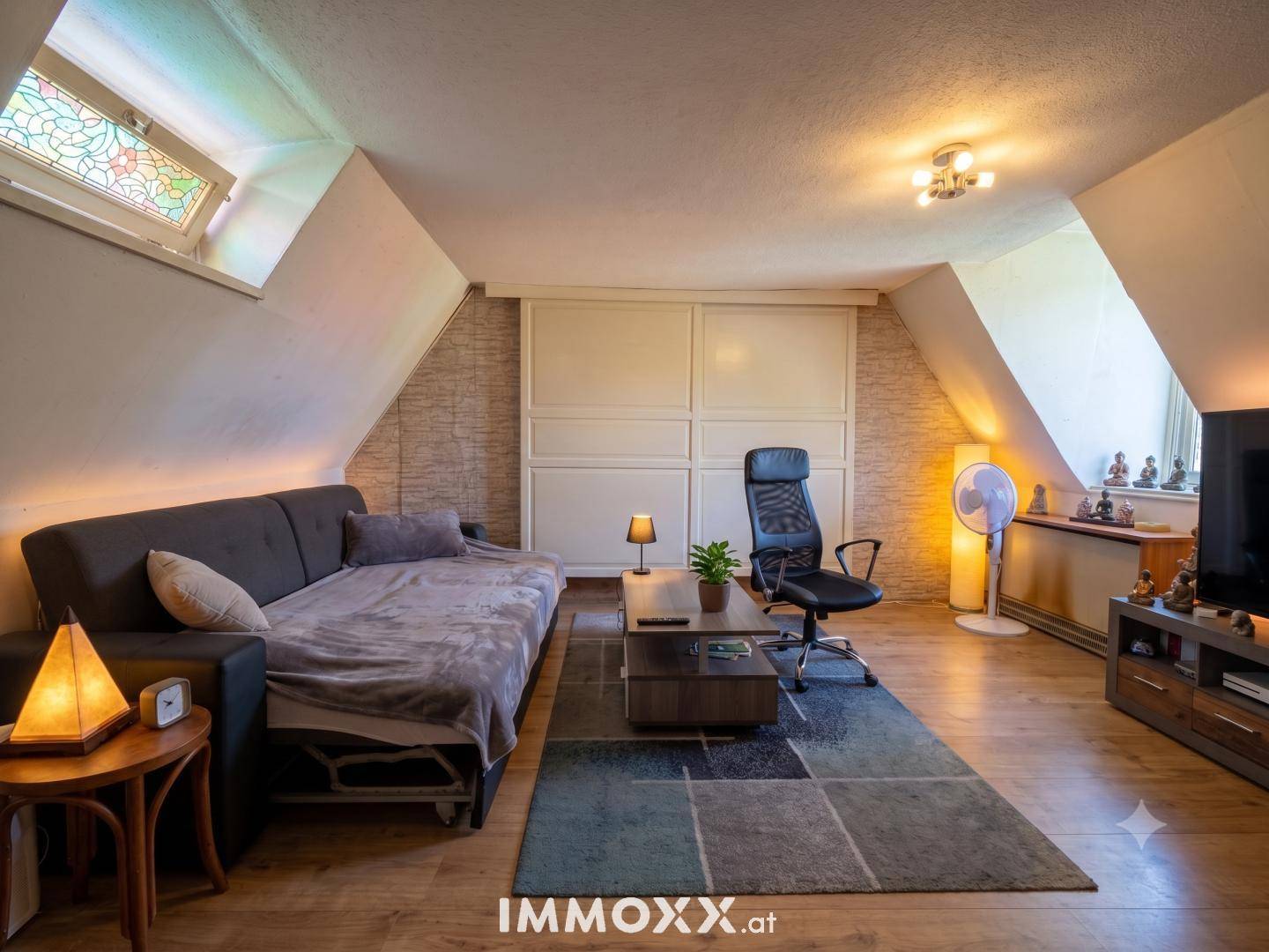 Gemütliches Dachgeschoss-Wohnzimmer mit Schlafsofa, Schrägen und einem bunten Teppich, ideal zum Entspannen.