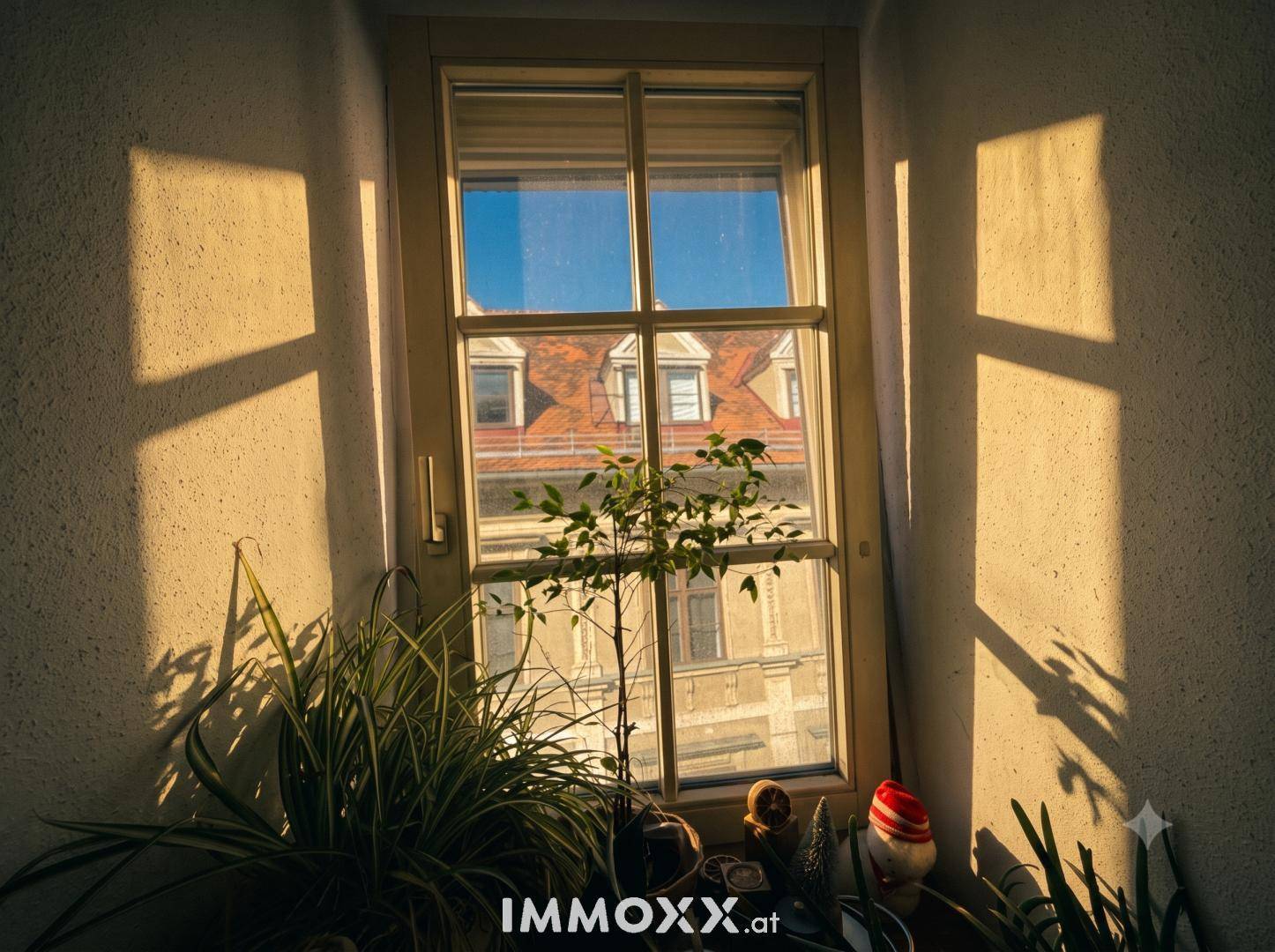 Sonnenlicht durchflutet ein Fenster und wirft Schatten auf die Wand, mit Blick auf ein gegenüberliegendes Dach.
