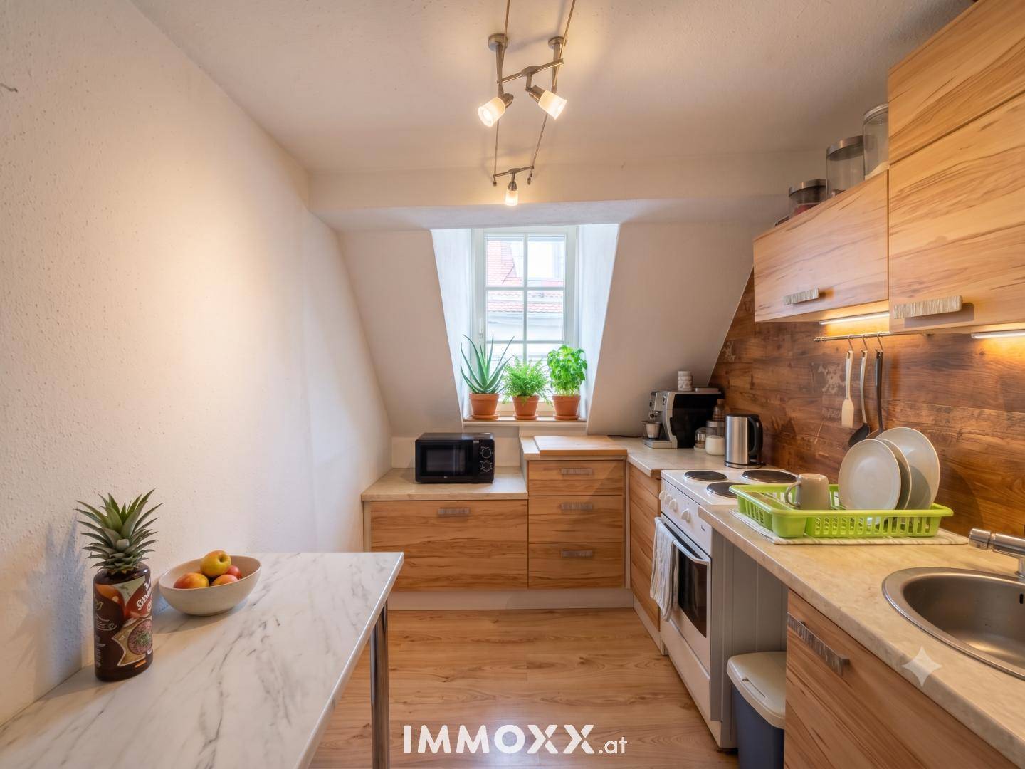 Gemütliche Dachgeschossküche mit Holzfronten, Fenster und integrierten Geräten, ideal für kleine Haushalte.