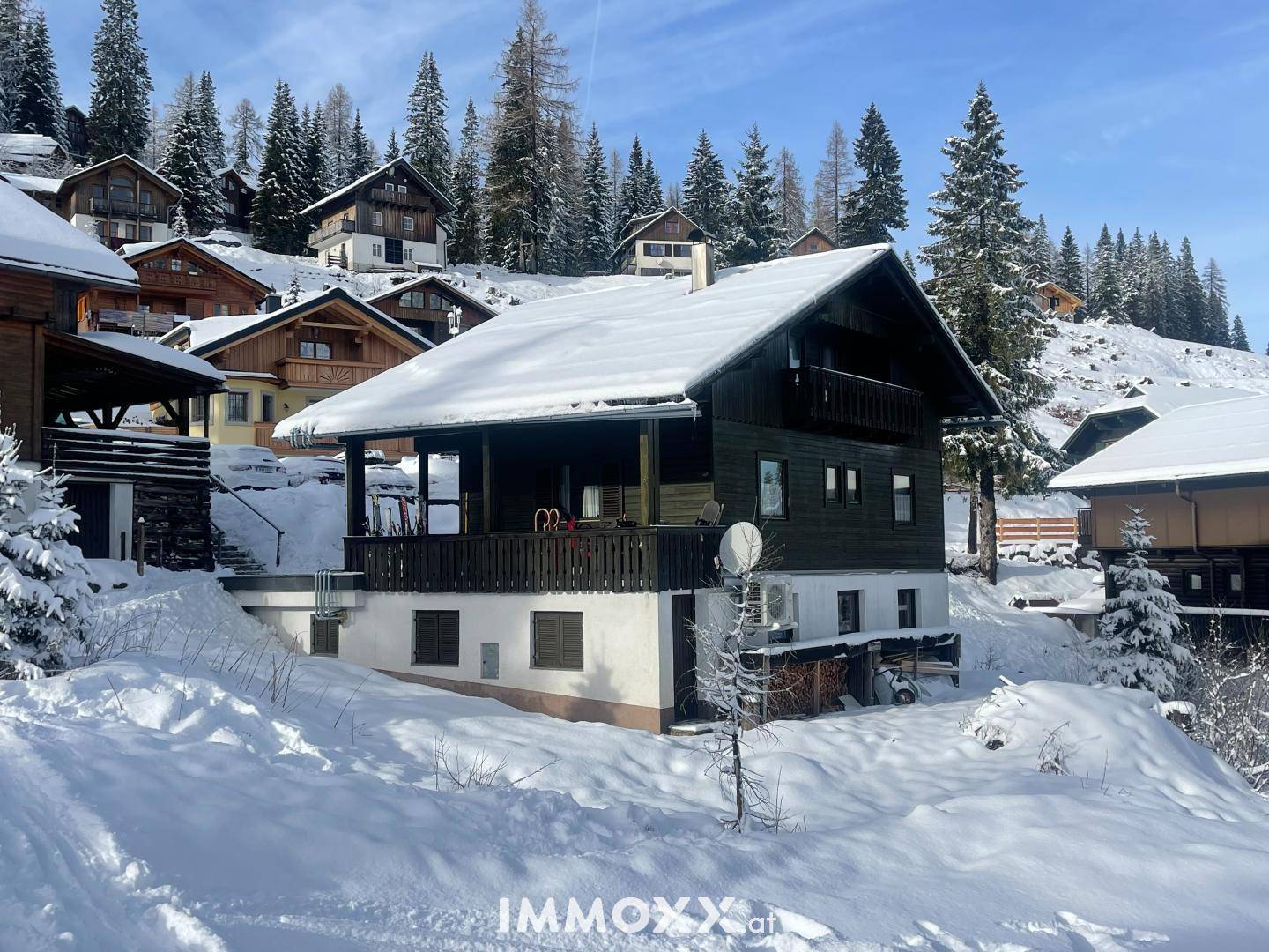 Traditionelles Holzchalet im Winter, umgeben von tiefem Schnee und verschneiten Tannenbäumen in den Bergen.