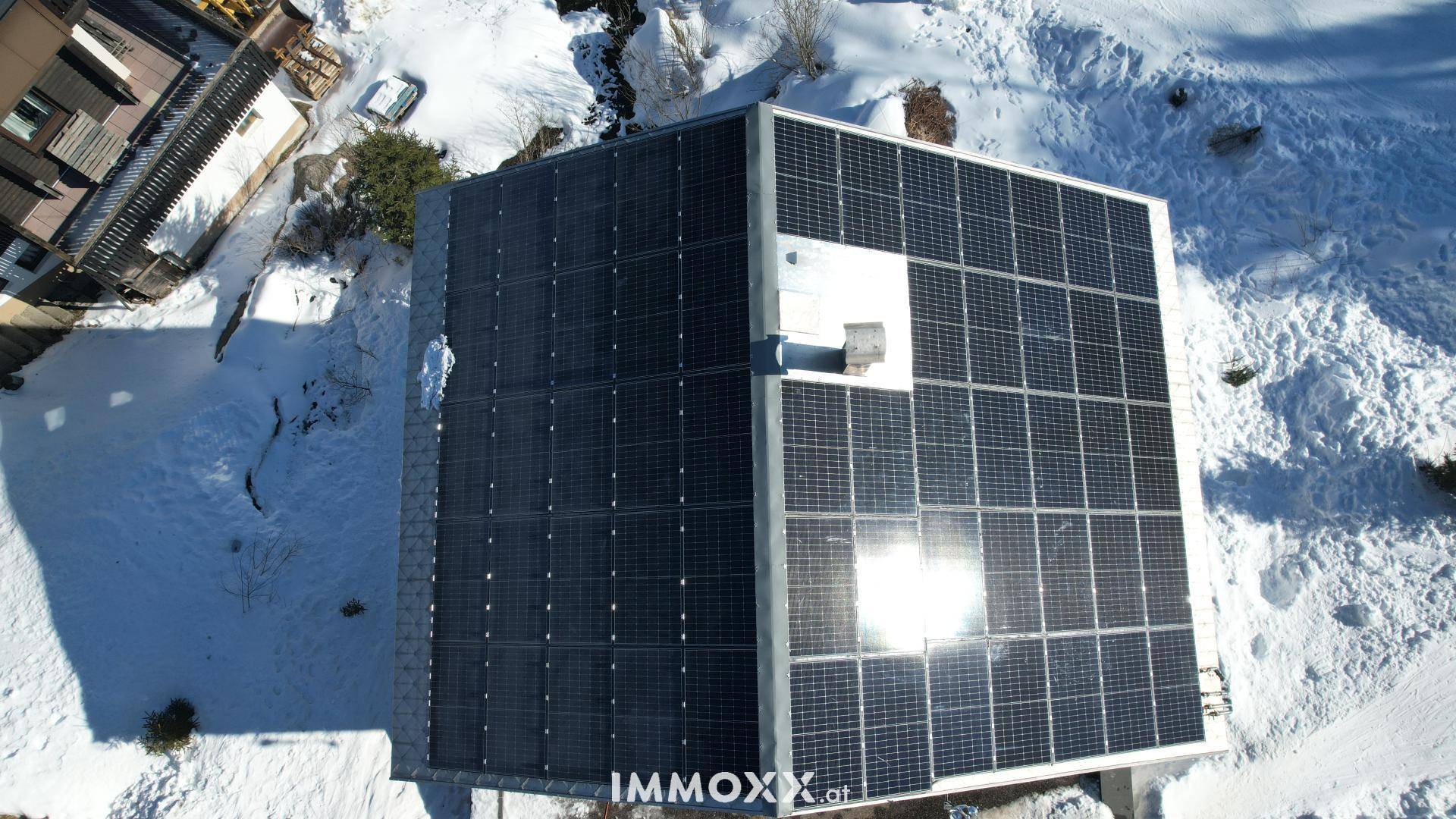 Detaillierte Luftaufnahme des Daches eines Chalets mit installierten Photovoltaik-Modulen im Winter.