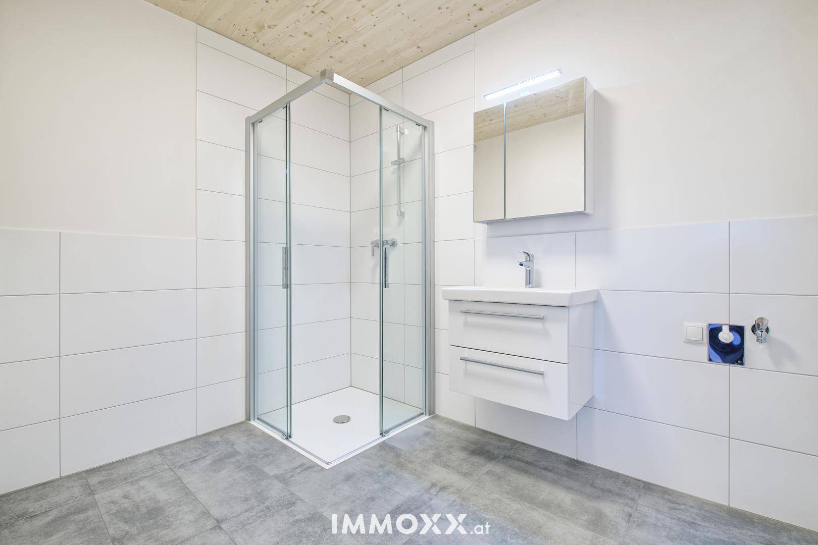 Helles Badezimmer mit Duschkabine, Waschtisch und Spiegelschrank, modern gefliest.