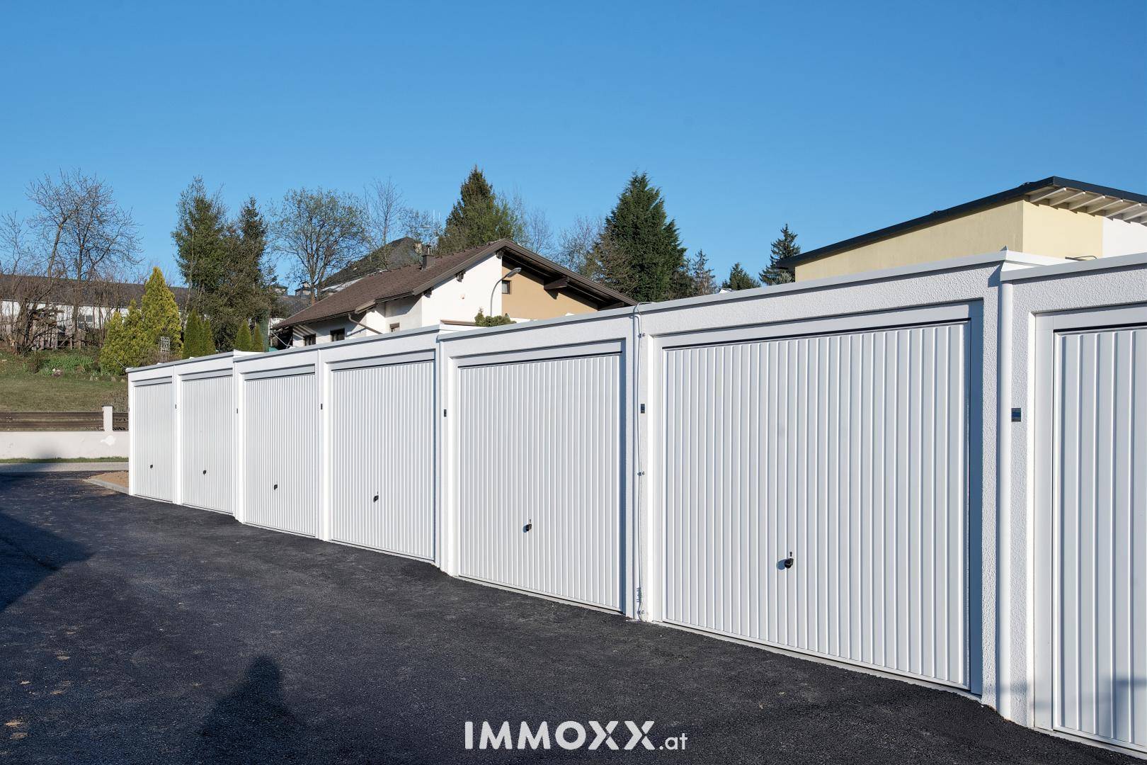 Eine Reihe moderner weißer Garagenboxen mit Wohnhäusern und Bäumen im Hintergrund.