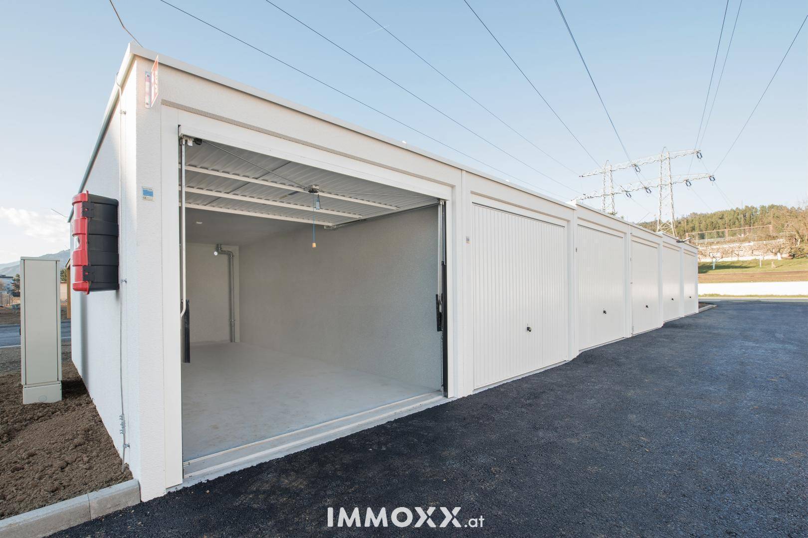 Eine offene, leere Garagenbox mit weiteren geschlossenen Einheiten unter klarem Himmel.