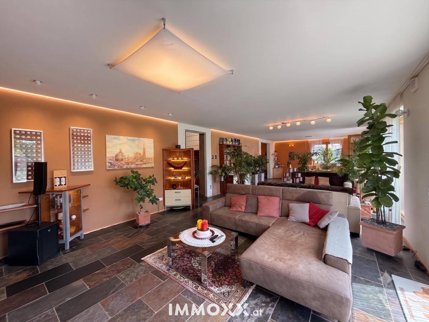 Großzügiges Wohnzimmer mit bequemen Sofas, dunklem Fliesenboden und vielen Pflanzen.