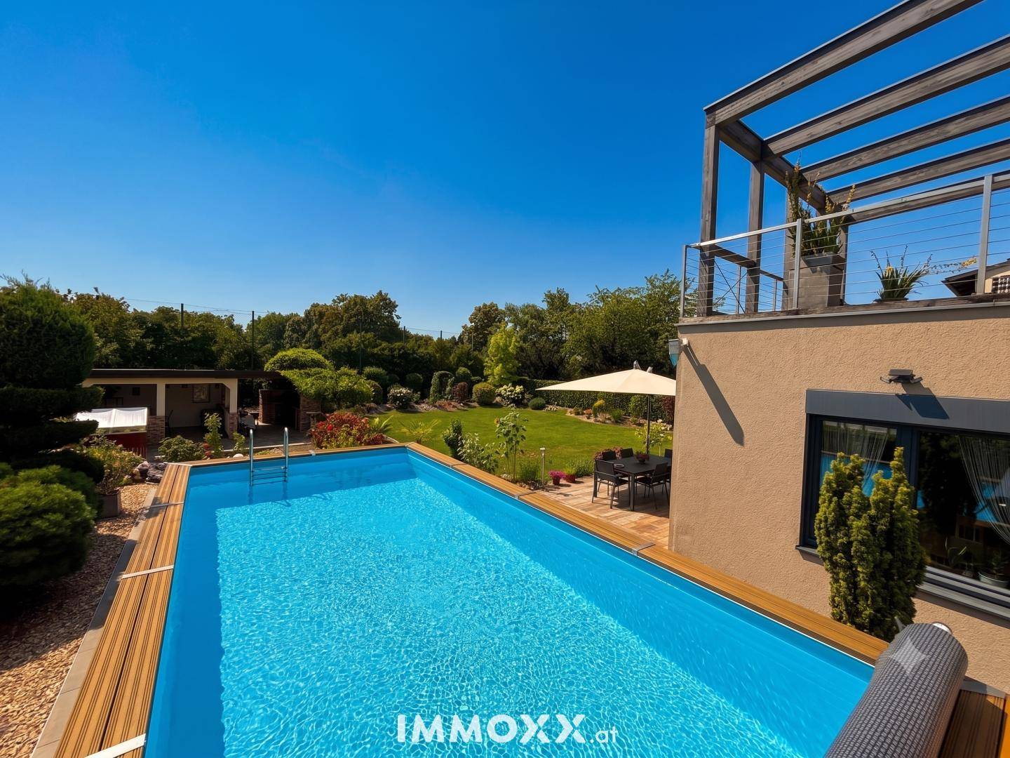 Erfrischender Poolbereich mit Holzdeck und Blick auf den weitläufigen Garten und die Terrasse.