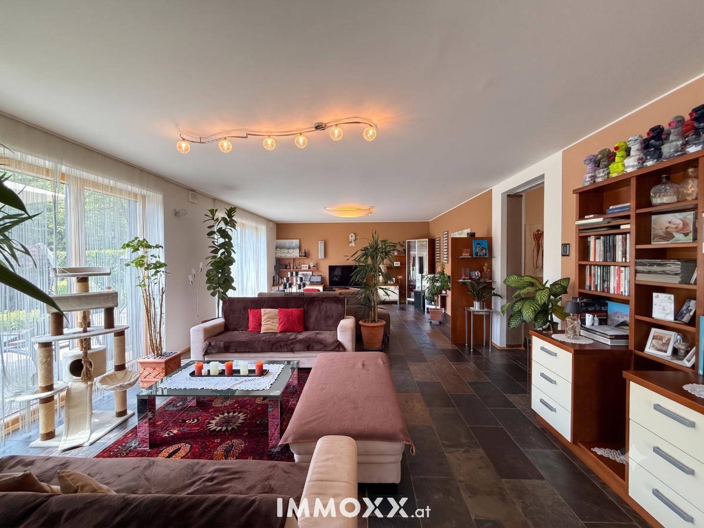 Gemütliches Wohnzimmer mit dunklem Fliesenboden, bequemen Sofas und Blick ins Grüne.