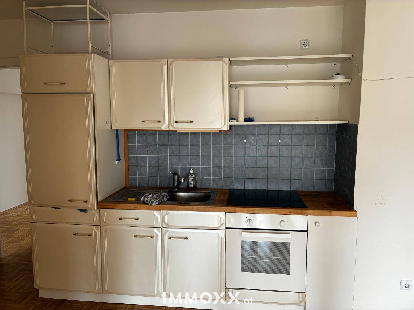 Kleine Einbauküche mit hellen Schränken, Holz-Arbeitsplatte und integrierten Geräten.