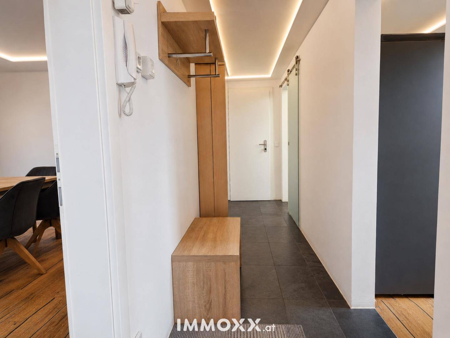 Heller Flur mit Garderobe, Sitzbank und dunklem Fliesenboden.