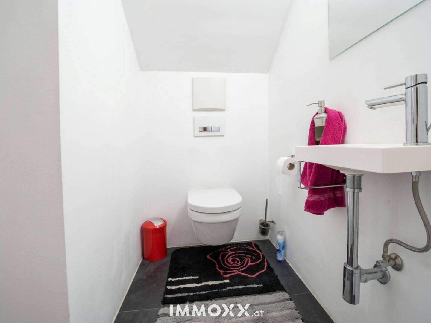 Separates Gäste-WC mit wandhängender Toilette, kleinem Waschbecken und dunklem Fliesenboden.