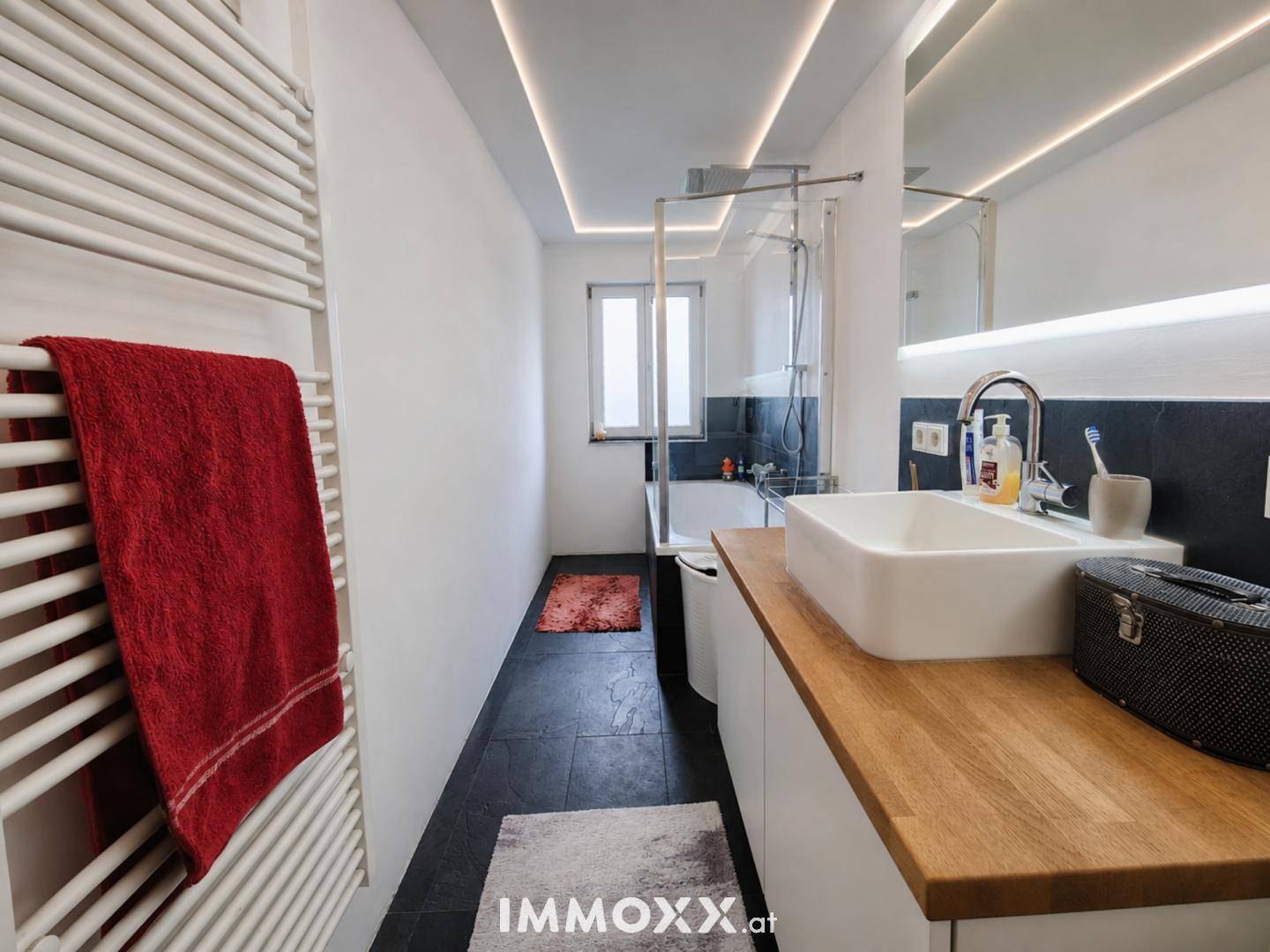Modernes Badezimmer mit Badewanne, Dusche, Einzelwaschbecken und beheiztem Handtuchhalter.