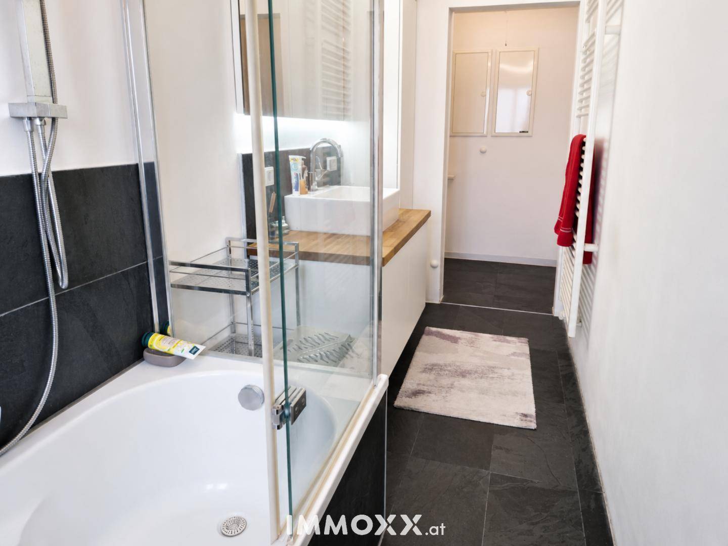 Modernes Badezimmer mit Badewanne, Duschabtrennung und dunklem Fliesenboden.