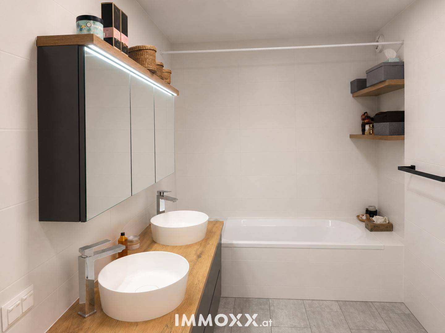 Modernes Badezimmer mit Badewanne, Doppelwaschbecken und beleuchtetem Spiegelschrank.