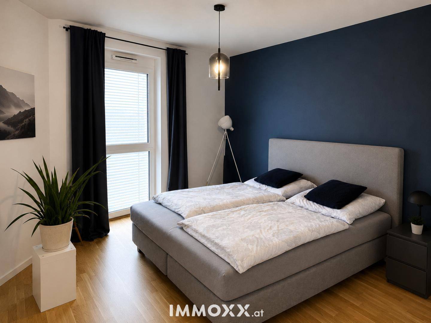 Schlafzimmer mit Doppelbett, Holzboden und einer dunkelblauen Akzentwand.