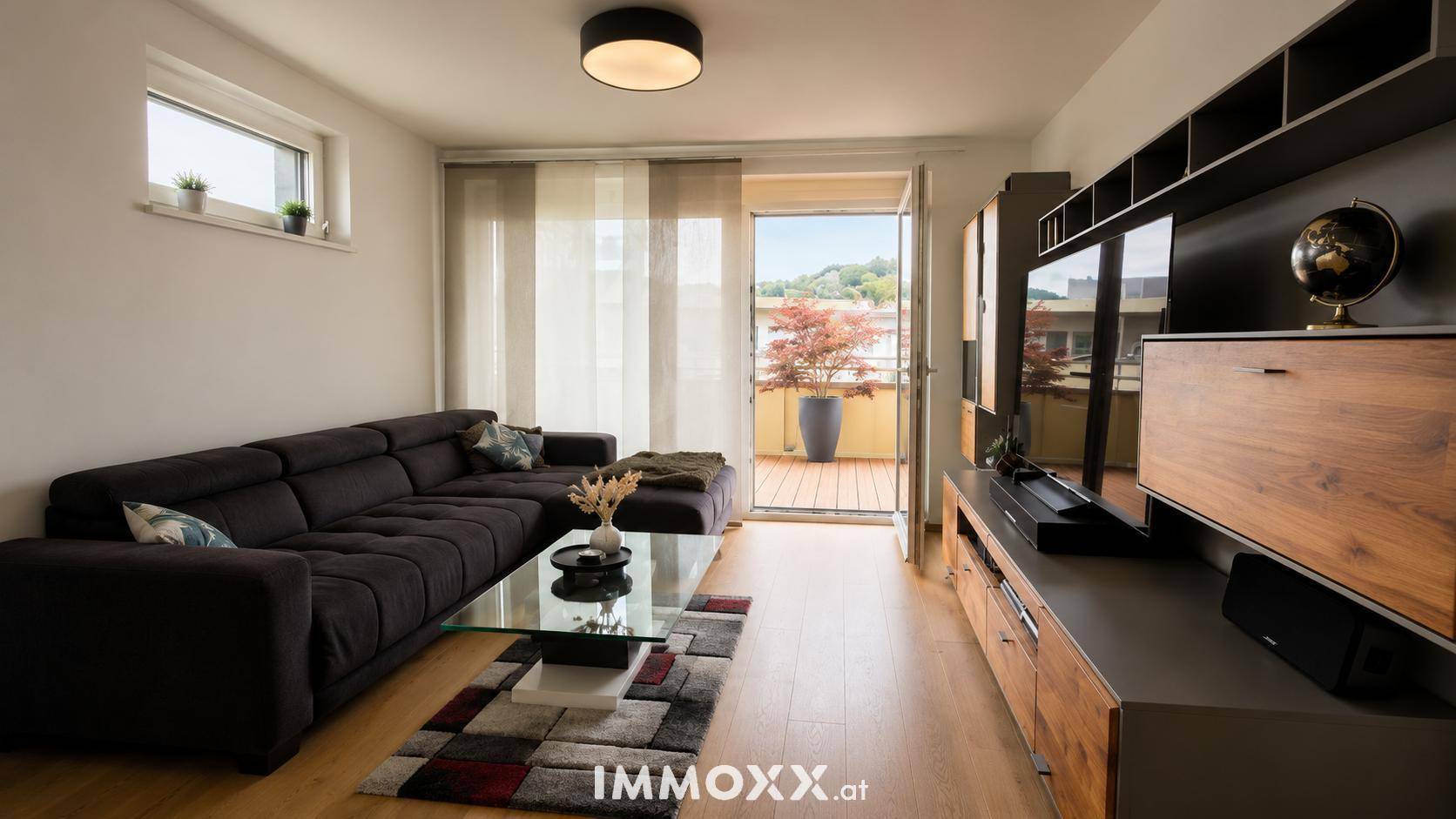 Gemütliches Wohnzimmer mit dunklem Sofa, TV-Möbel und direktem Zugang zum Balkon.