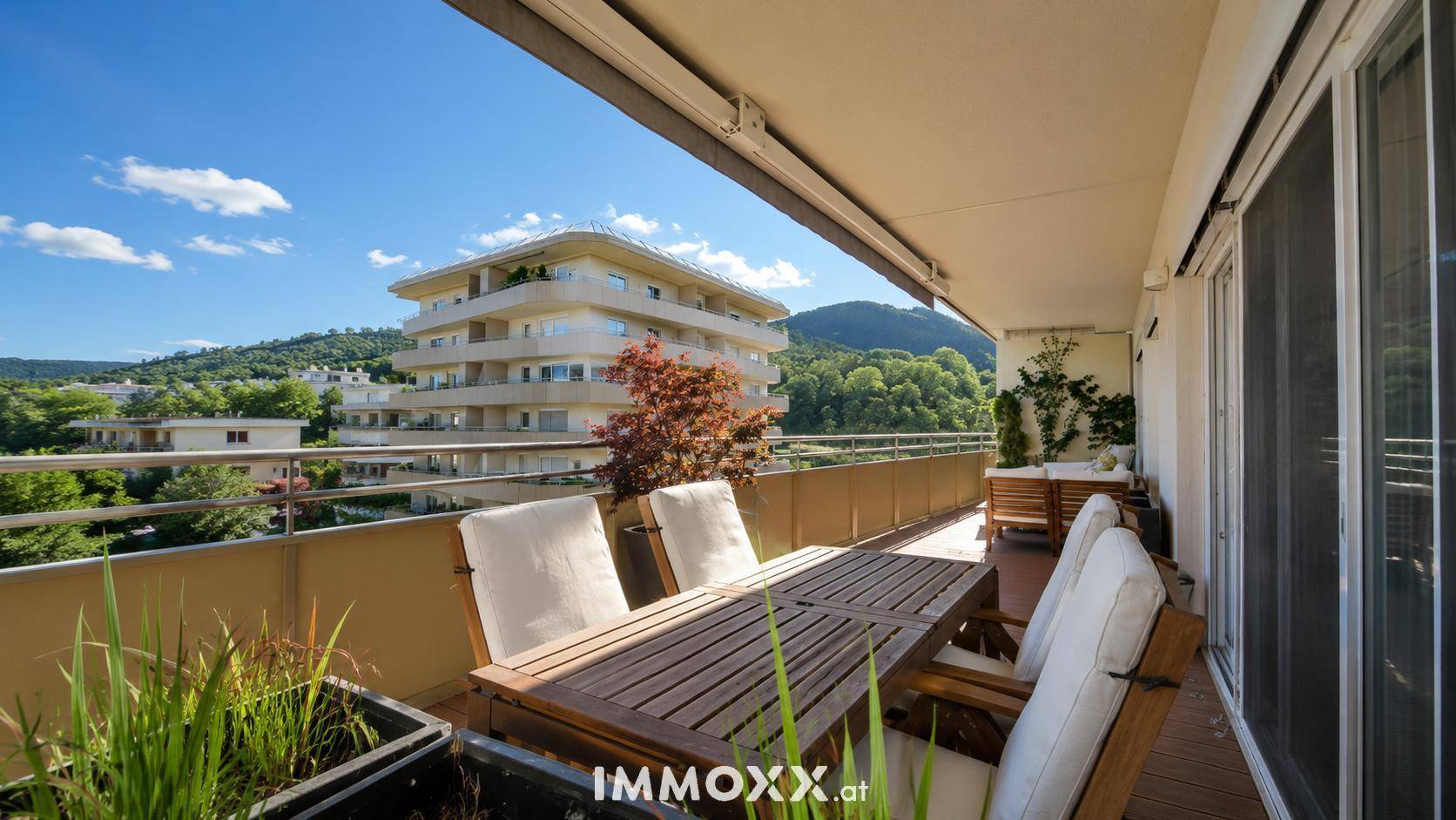 Geräumiger Balkon mit Esstisch, Pflanzen und Blick auf die umliegende Landschaft und Gebäude.