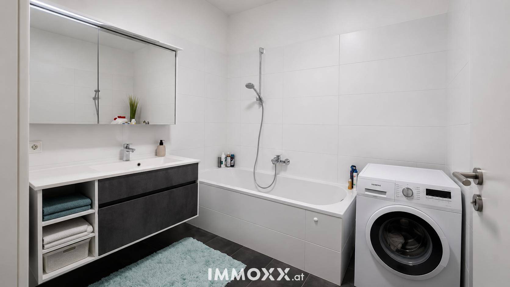 Modernes Badezimmer mit Badewanne, Einzelwaschbecken, Spiegelschrank und Waschmaschine.