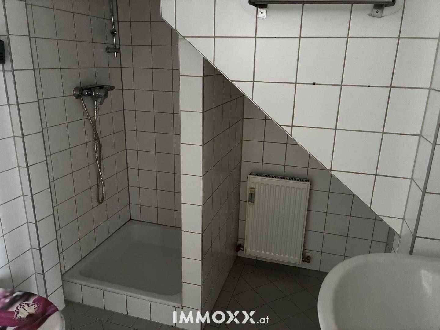 Badezimmer mit Duschkabine, weißen Fliesen und Heizkörper unter der Dachschräge.
