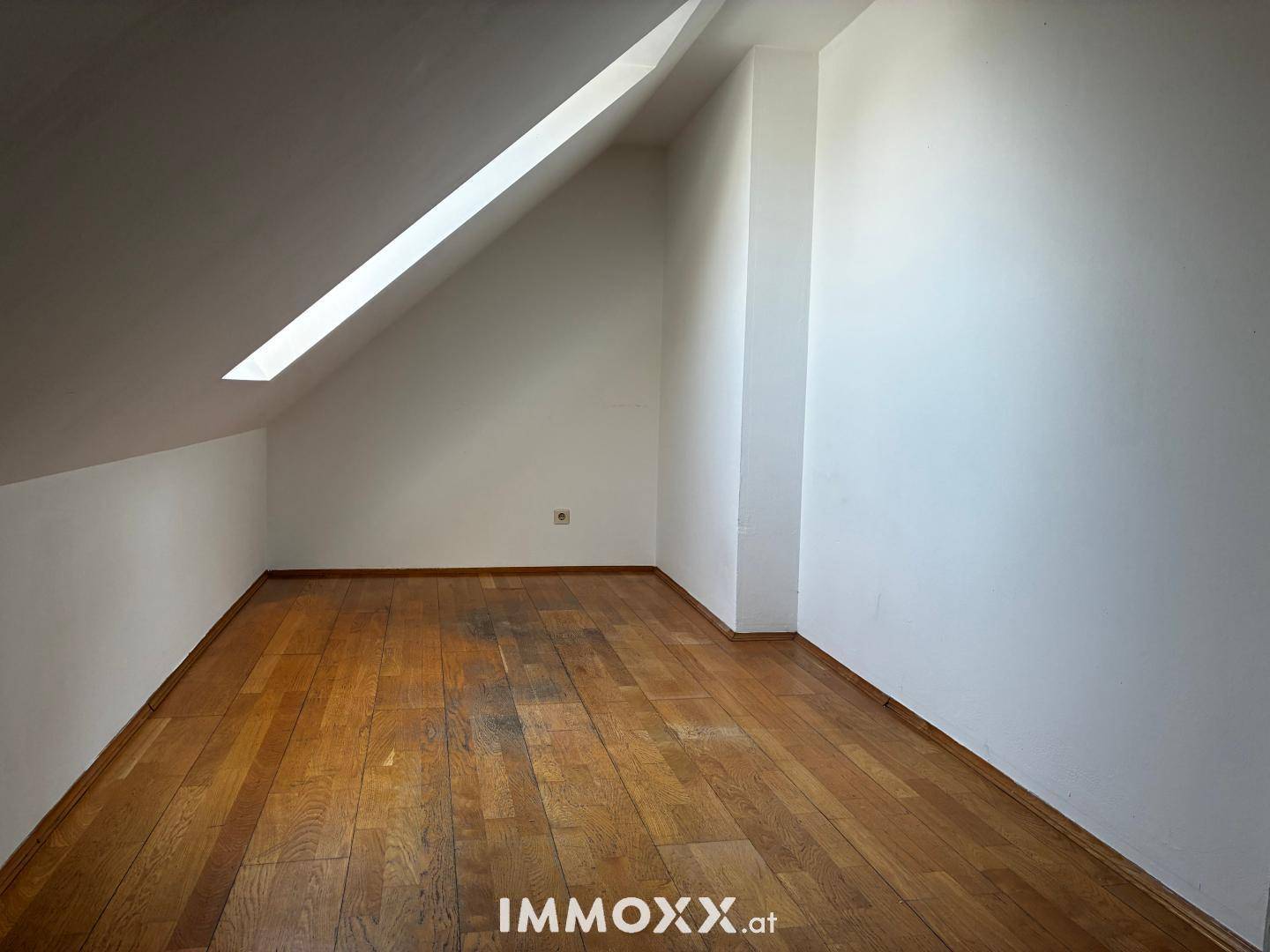 Dachgeschossraum mit schräger Decke, Dachfenster und Holzparkettboden, bietet natürliches Licht.