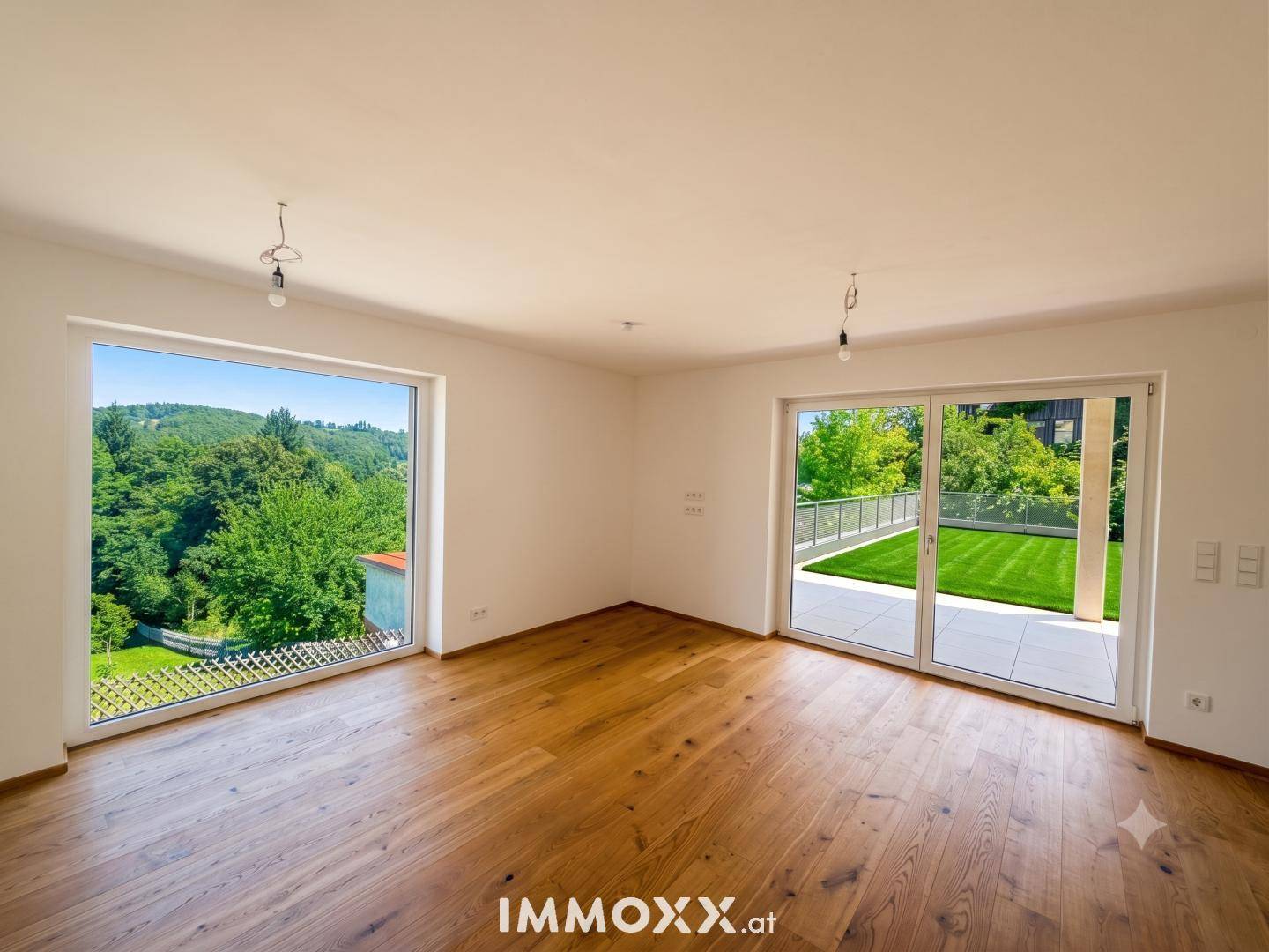 Heller Wohnraum mit großen Fenstern, Holzboden und Zugang zu einer Terrasse.