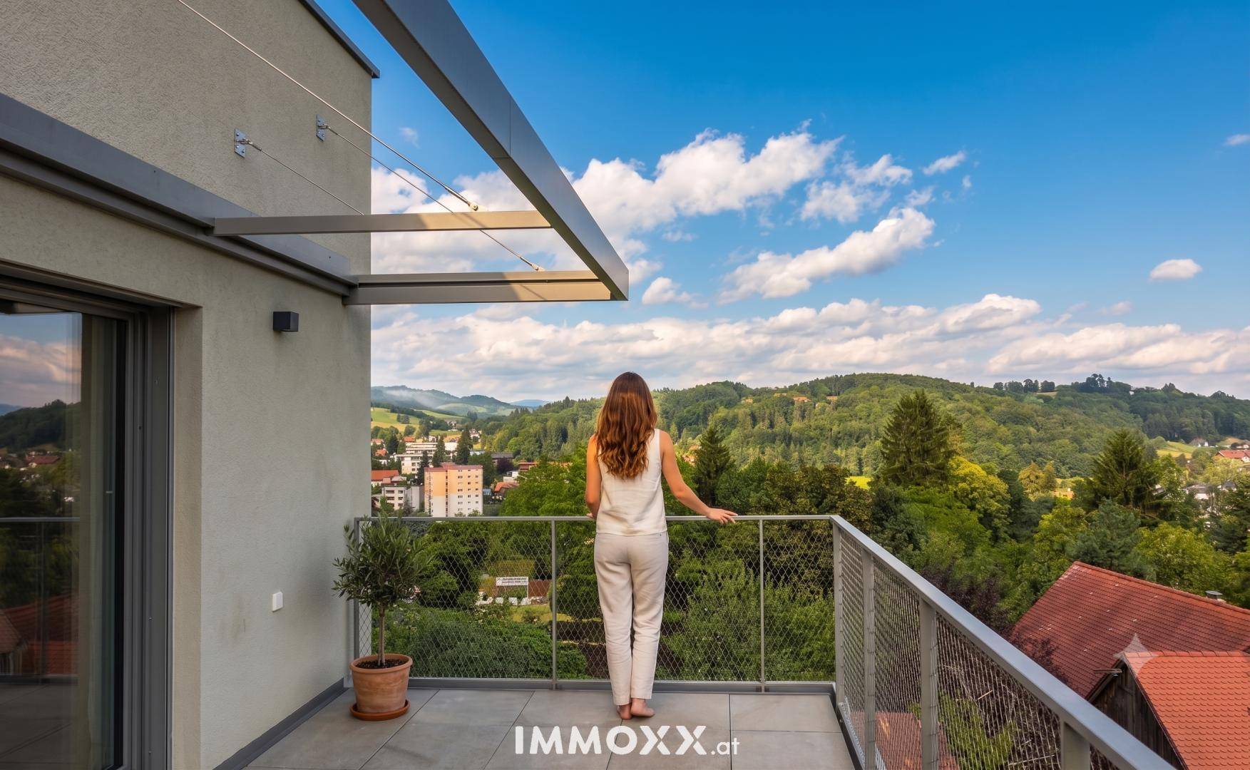 Frau genießt den weiten Blick über die grüne Hügellandschaft von einem modernen Balkon.