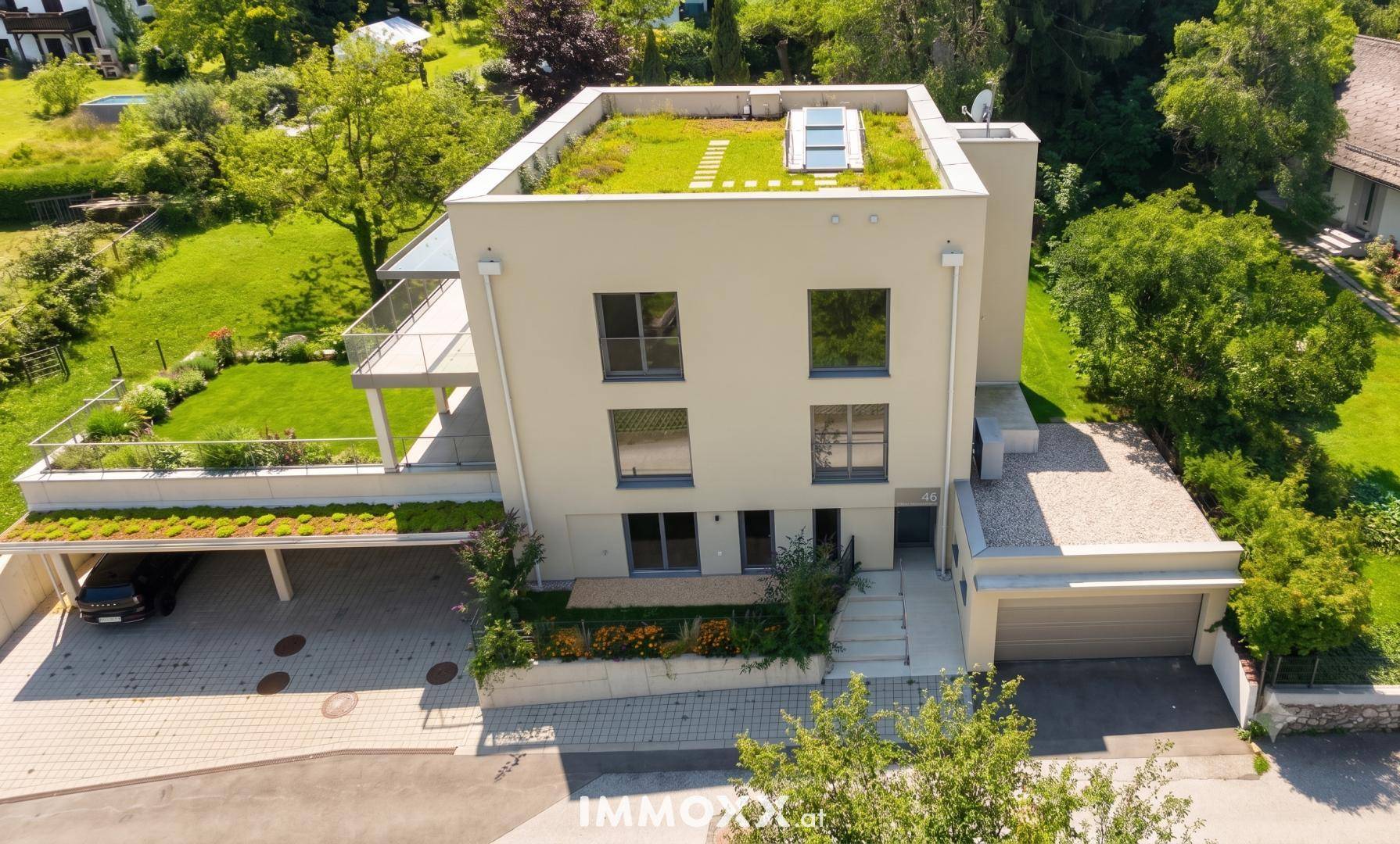 Modernes Wohnhaus mit Flachdach, Gründach, Carport und Garage in grüner Umgebung.