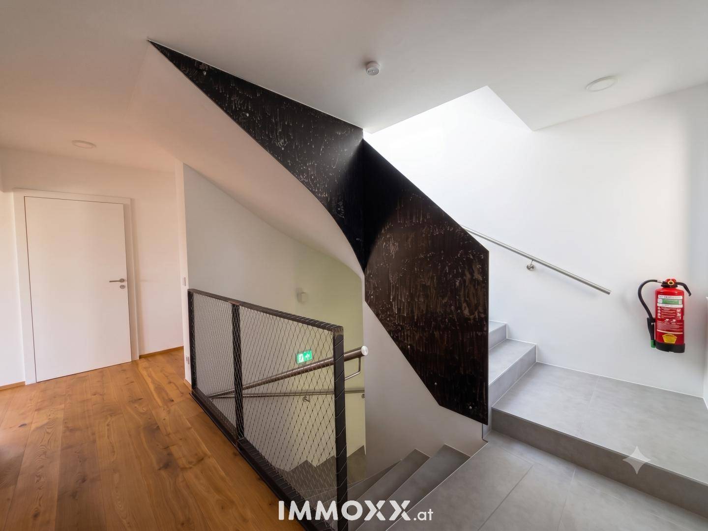 Modernes Treppenhaus mit Holzboden, Betontreppe und minimalistischem Metallgeländer.