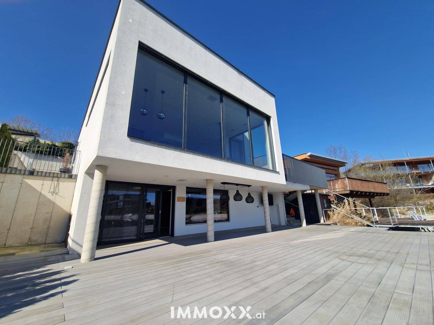 Moderne Architektur des Hauses mit großen Glasflächen und weitläufiger Holzterrasse am Wasser.