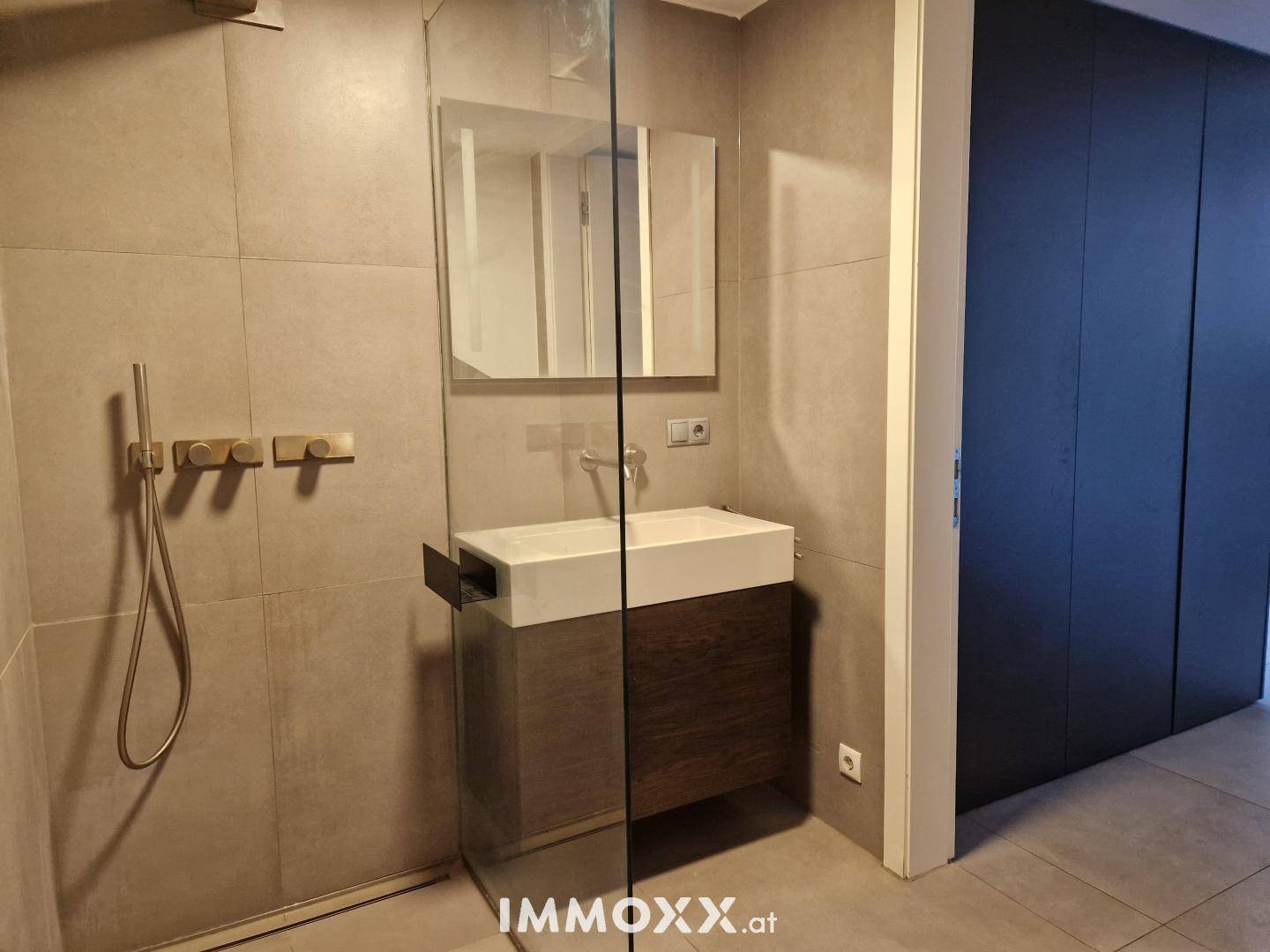 Modernes Badezimmer mit begehbarer Dusche, Einzelwaschbecken und grauen Fliesen an Wänden und Boden.