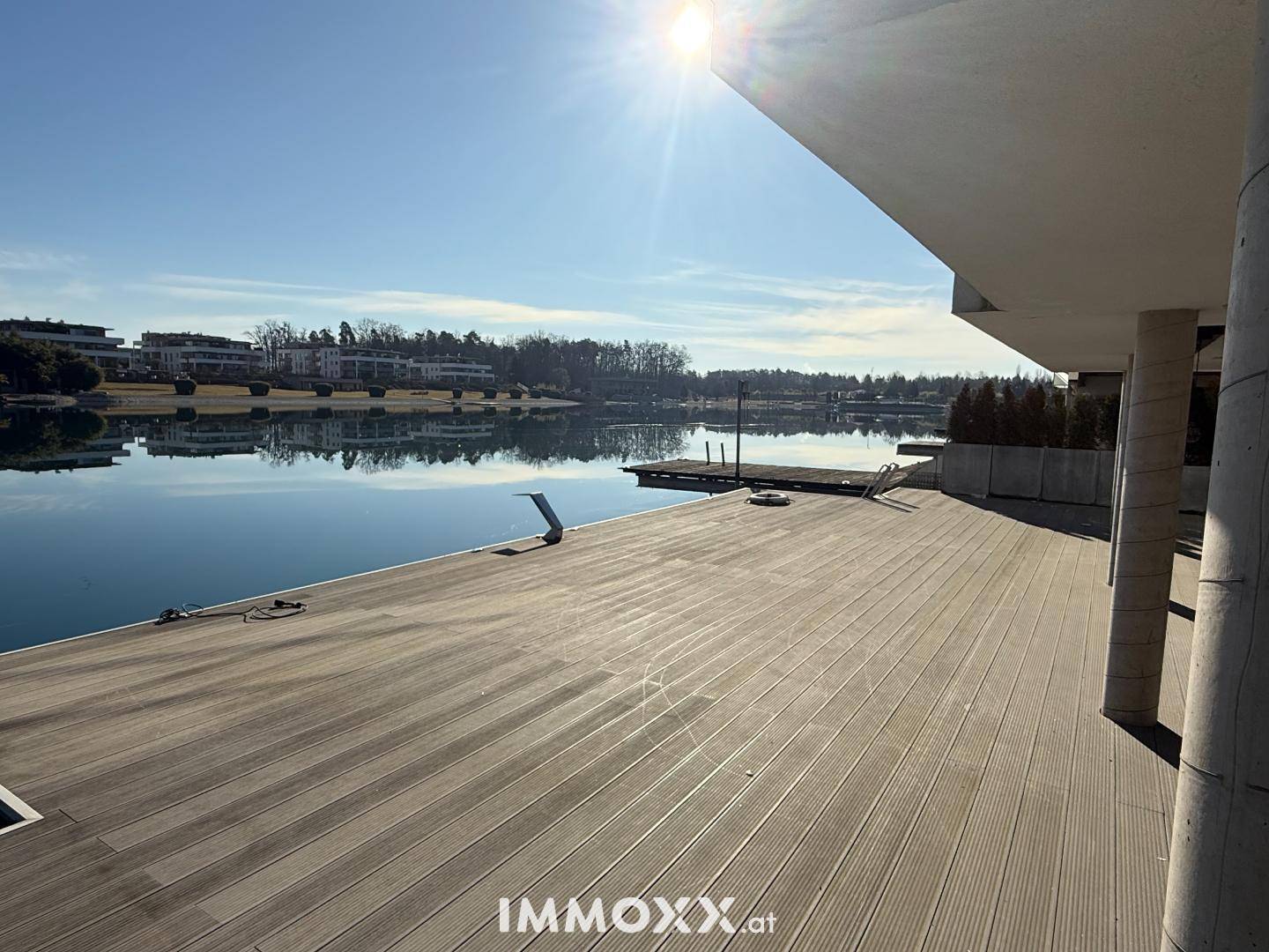 Sonnige Holzterrasse direkt am See mit weitem Blick über das Wasser und die Umgebung.