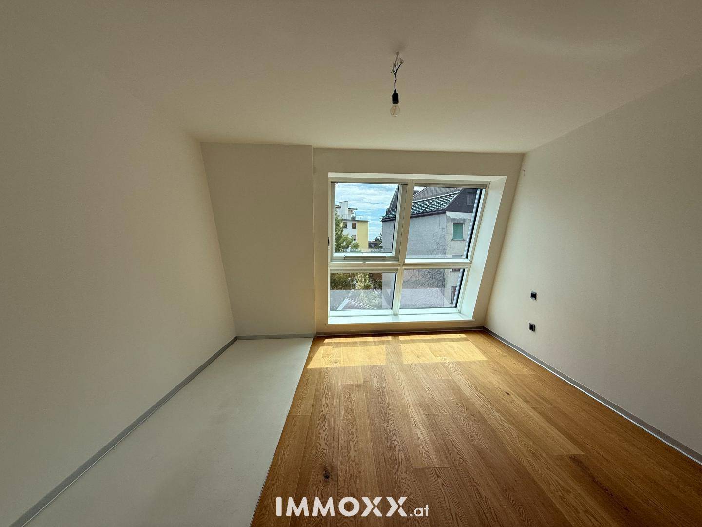 Helles Schlafzimmer mit Holzboden, weißen Wänden und einem großen, schrägen Fenster für viel Licht.