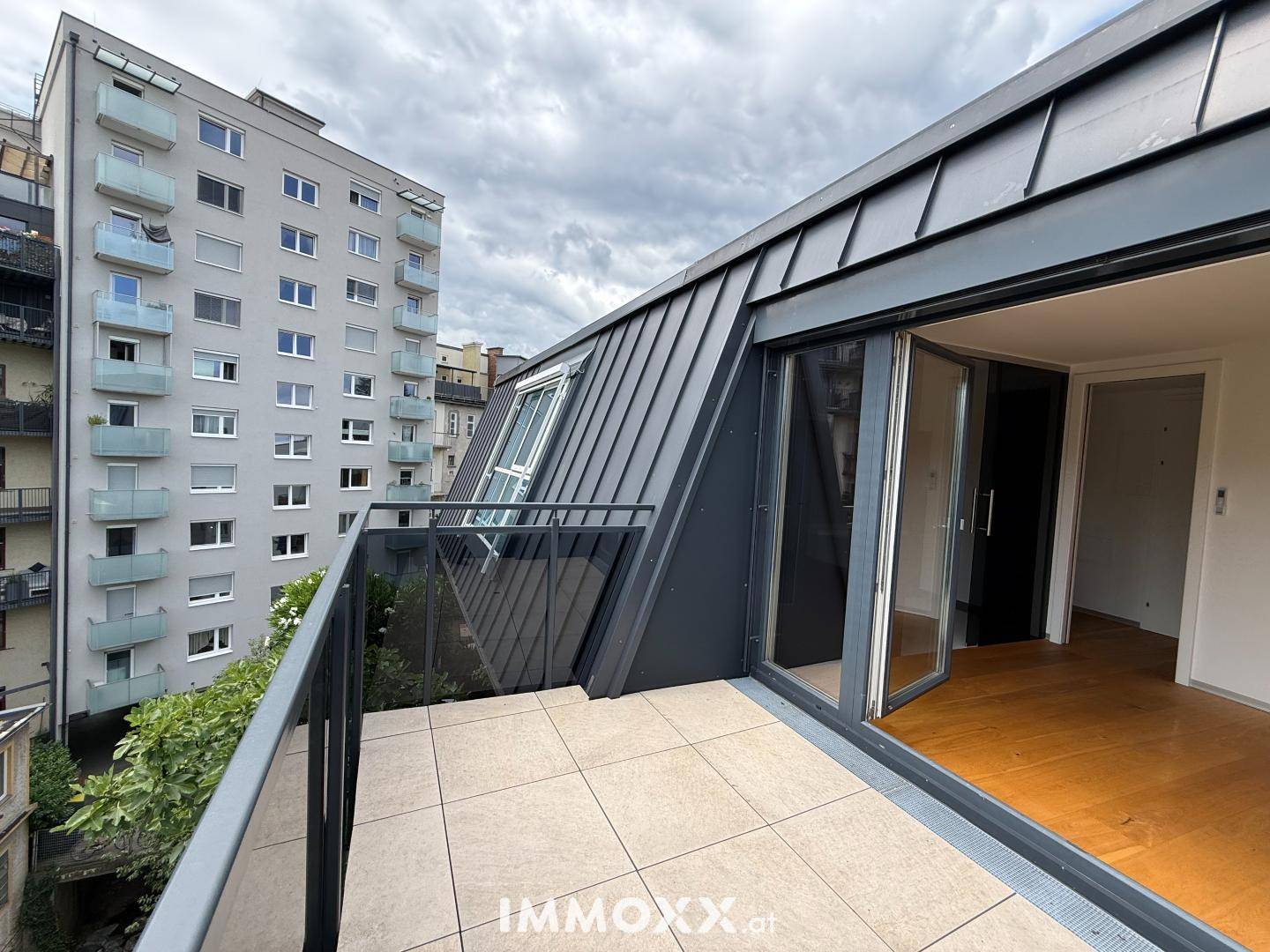 Balkon mit Fliesenboden und Blick auf die Stadtkulisse, charakterisiert durch eine moderne Dachschräge.