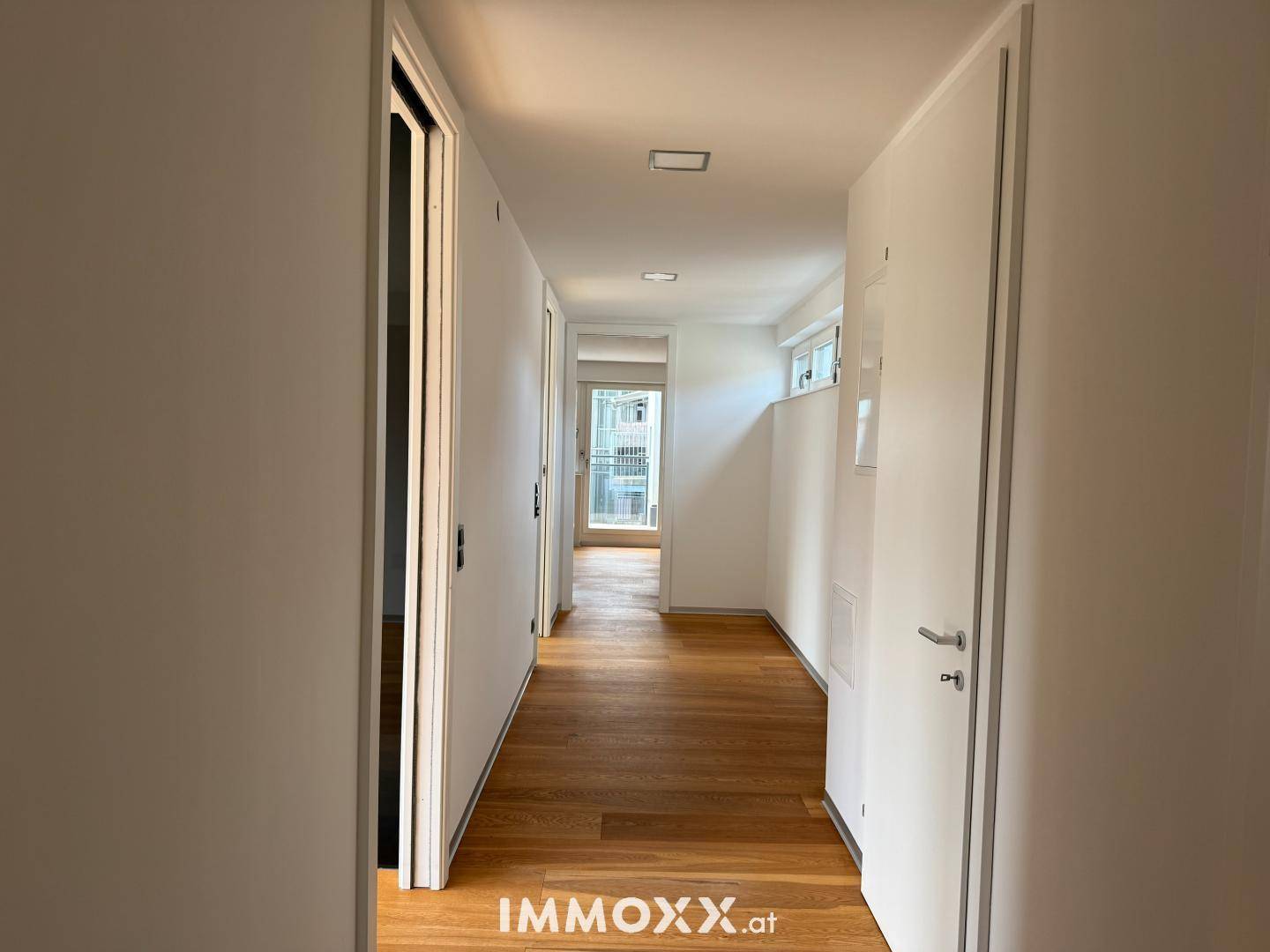 Heller Flur mit Holzboden und weißen Wänden, der zu den verschiedenen Räumen der Wohnung führt.