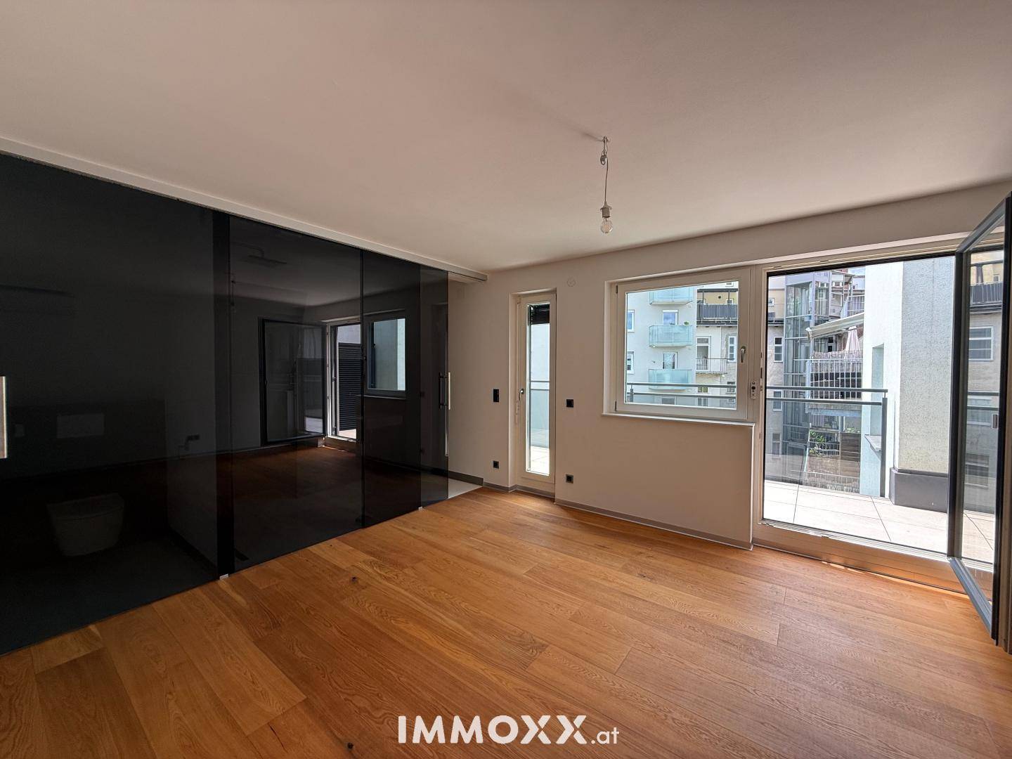 Geräumiges Schlafzimmer mit Holzboden, großen Glasfronten und direktem Zugang zum Balkon.